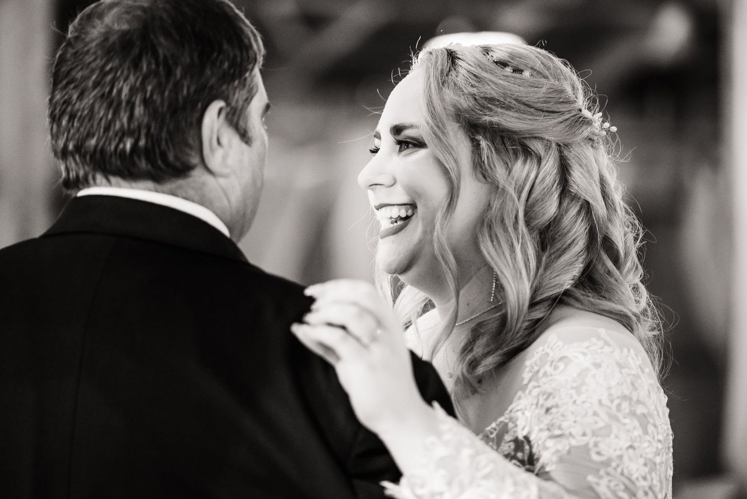 Black and white candid photo captures joyful laughter during wedding dance.