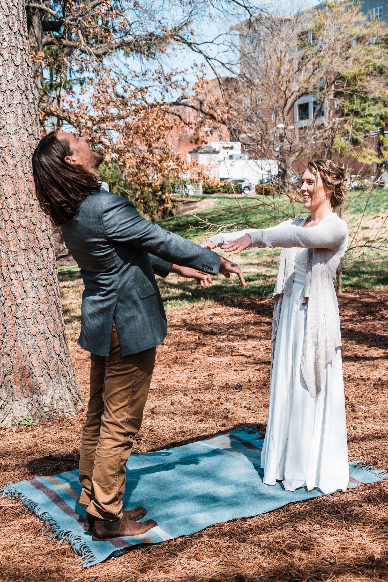 A couple dancing playfully on a blue blanket during an outdoor wedding ceremony.