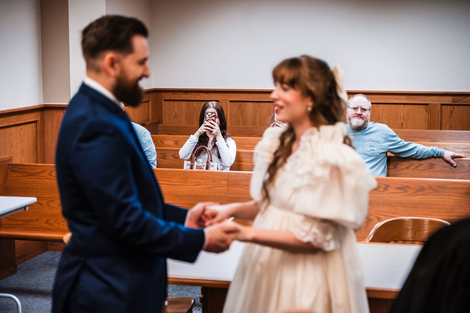 Couple holds hands during intimate courthouse wedding ceremony with guests in background.