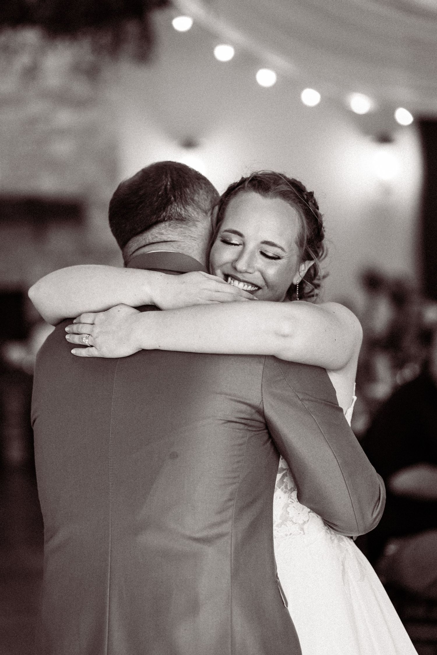 Joyful bride embracing groom during emotional first dance at wedding reception in black and white.