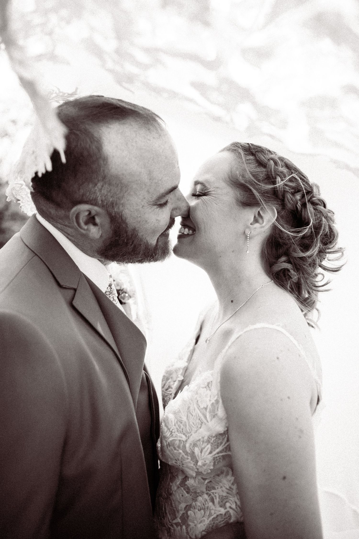 Black and white photo of bride and groom sharing first kiss at outdoor wedding ceremony.