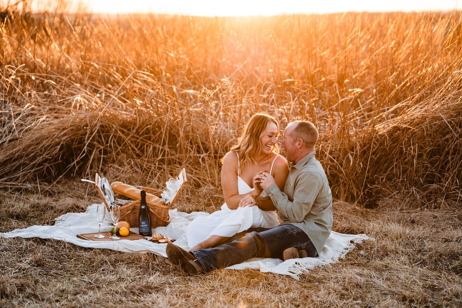 A couple enjoys a romantic sunset picnic on a blanket in a golden wheat field during summer.