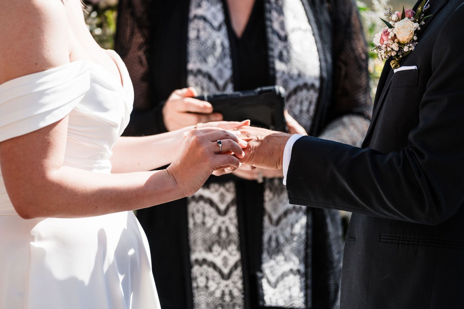 Close-up of bride and groom exchanging rings during outdoor wedding ceremony with officiant.