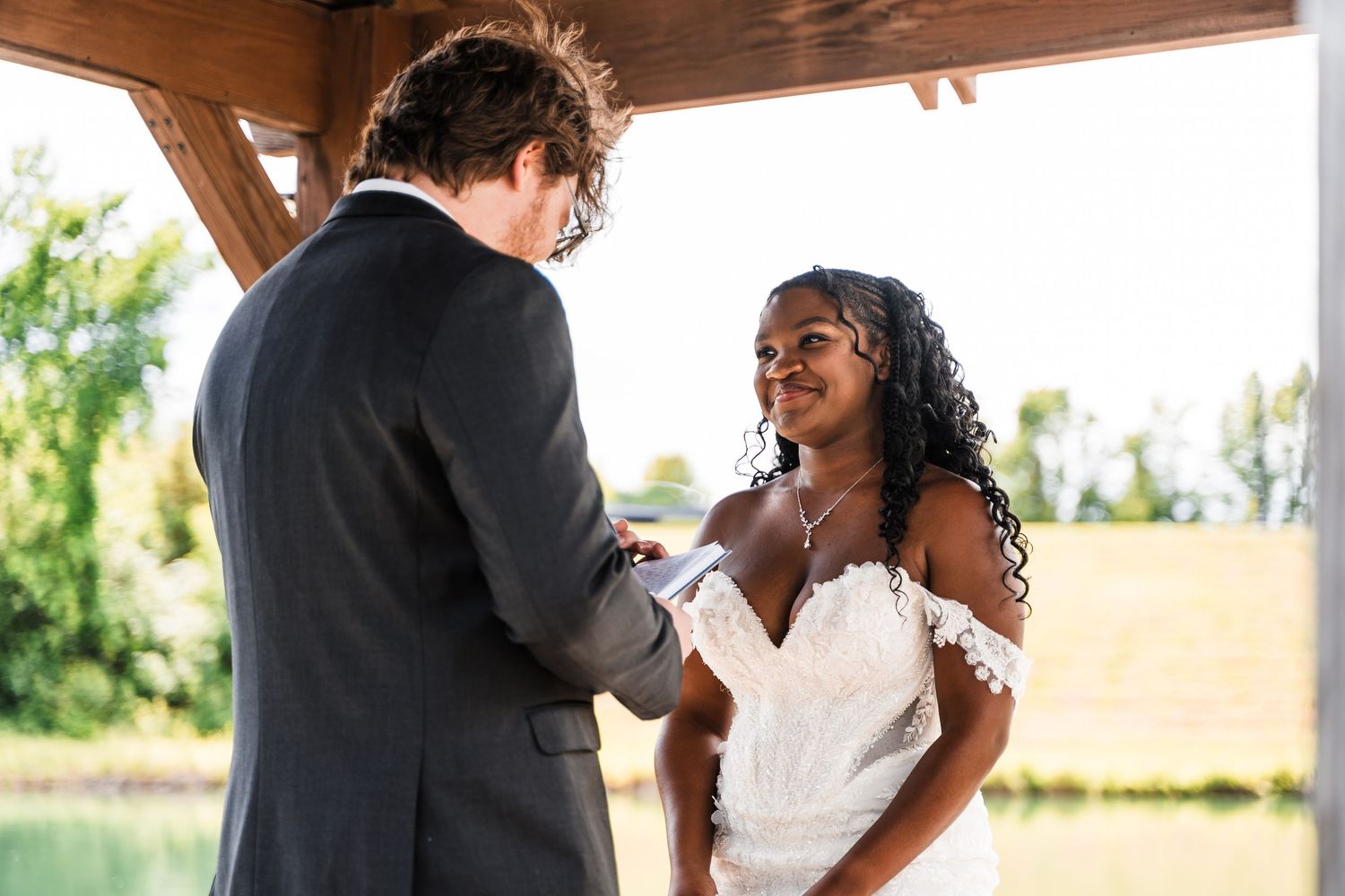 Interracial couple sharing a tender moment during wedding ring exchange ceremony outdoors.