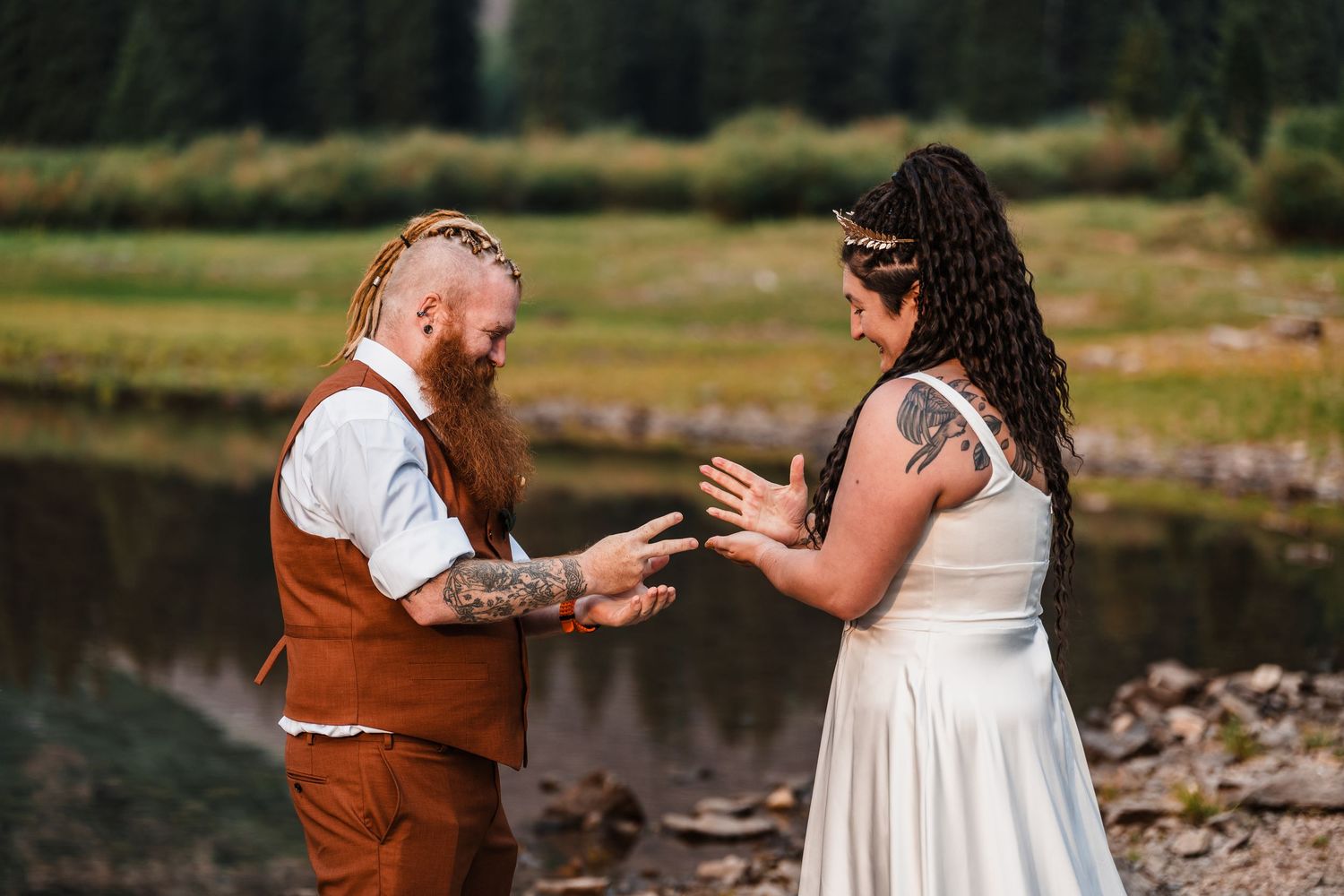 Tattooed couple exchanging vows outdoors by a forest lake during intimate mountain elopement.