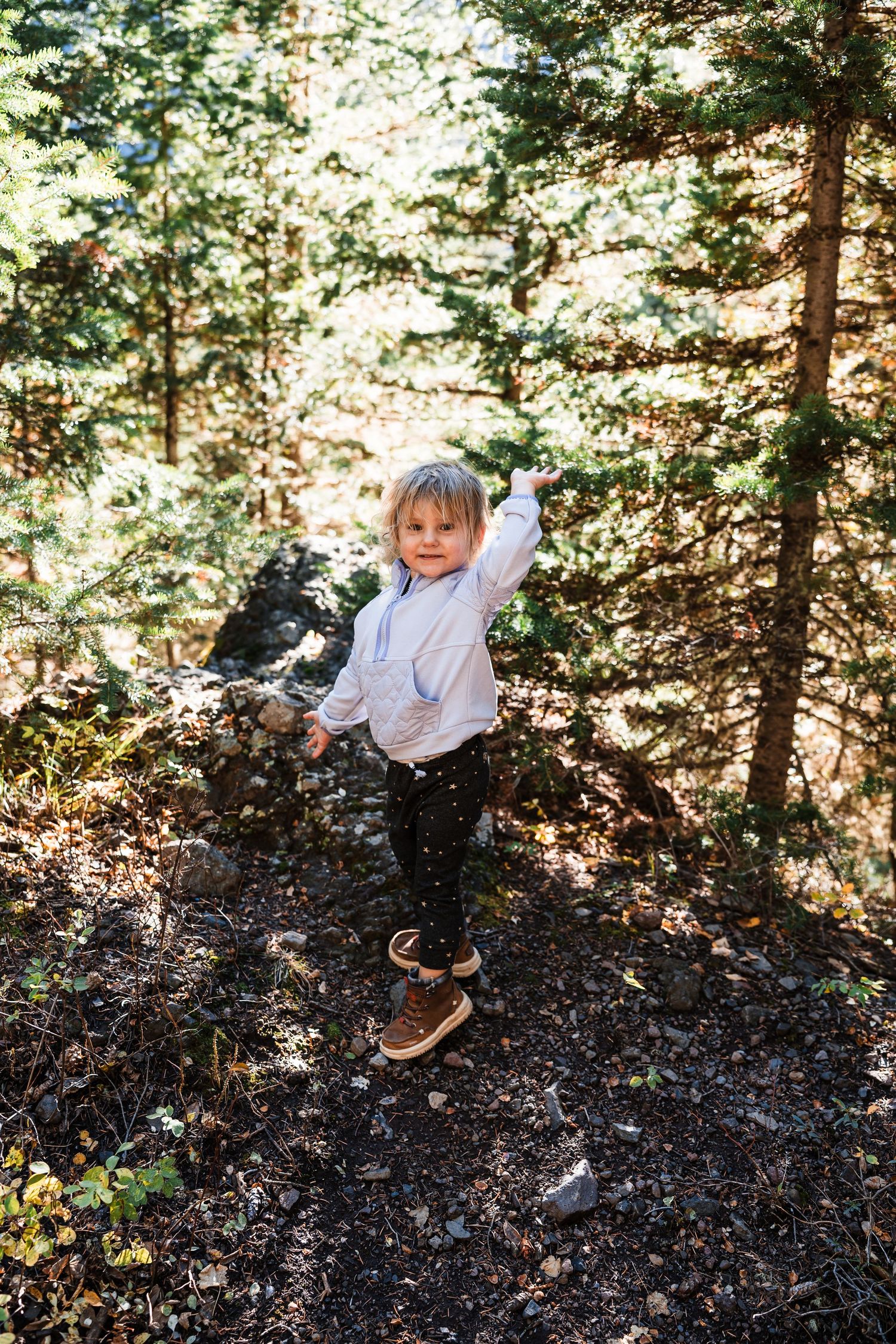 A child plays and rolls down a hill covered in fallen leaves on a sunny autumn day in the woods.