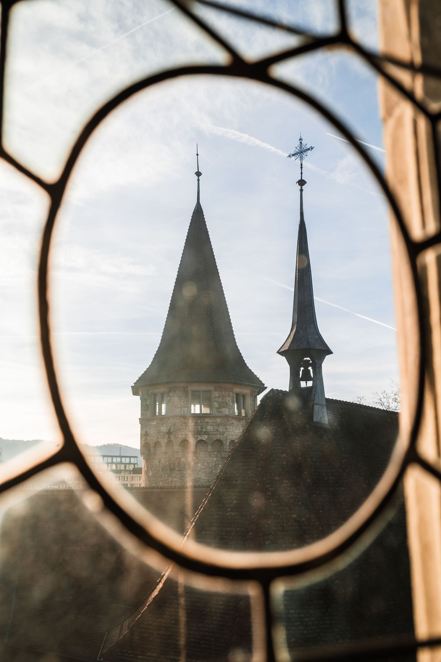 Gothic church spires and towers silhouetted through an ornate window frame at sunset.