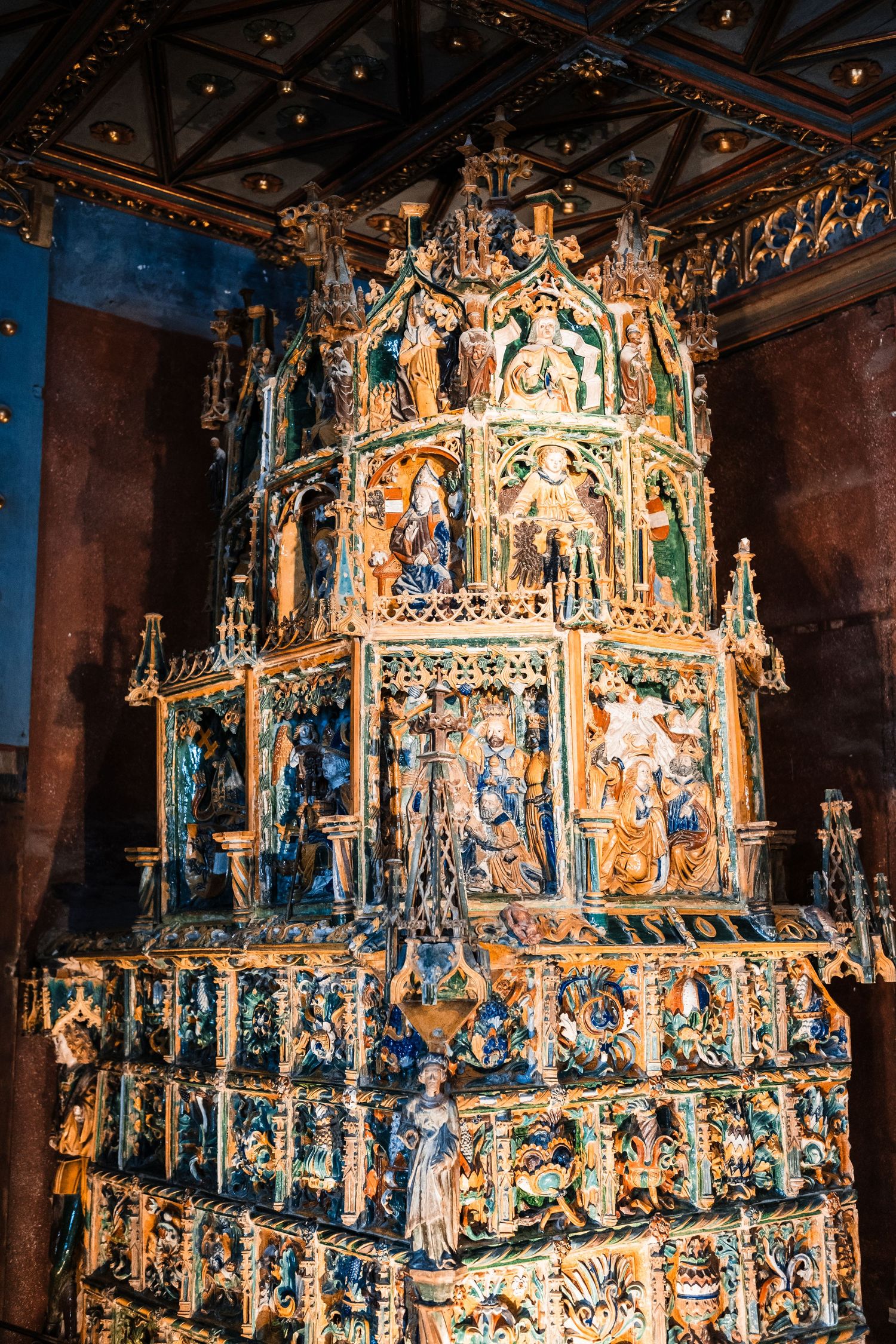 Intricately carved religious altarpiece with multiple tiers displaying colorful religious scenes and figures.