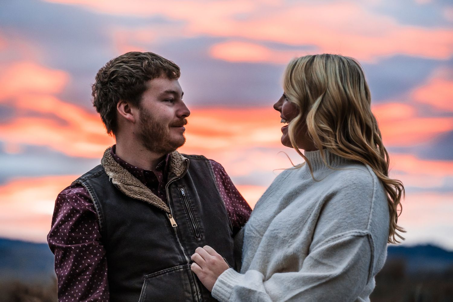 Two people share a romantic moment against a vibrant pink and orange sunset sky.