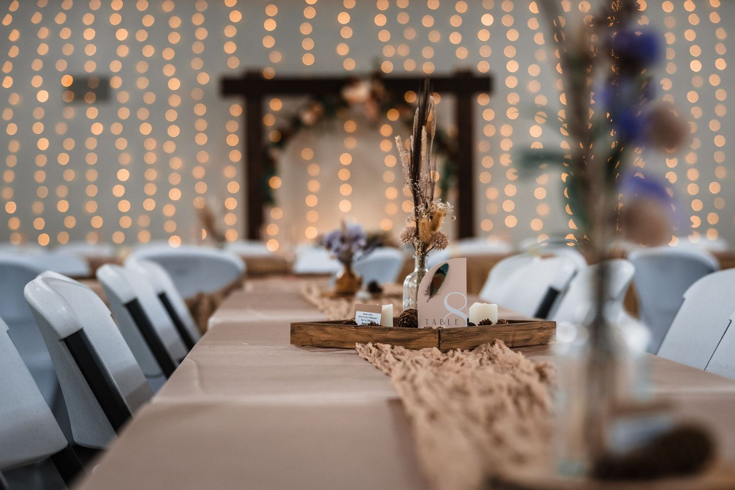 Elegant wedding reception tables decorated with string lights and white linens create a romantic ambiance.