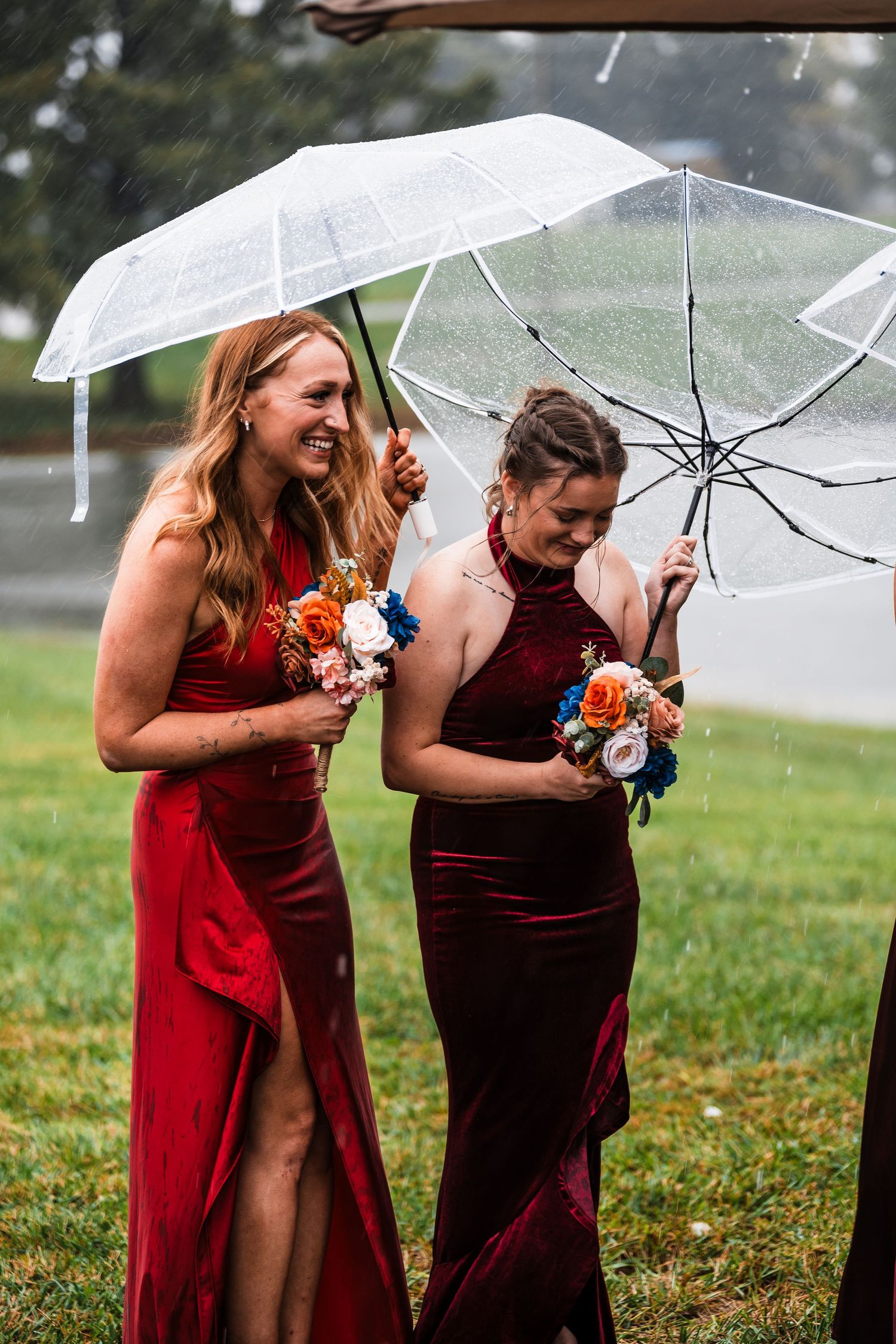 Bridesmaids in burgundy dresses share laughs under clear umbrellas on a rainy day.