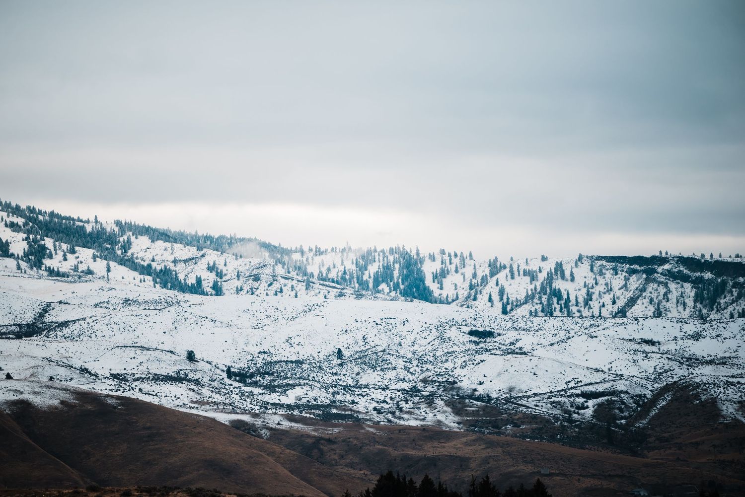 Snow-covered mountains and slopes under an overcast sky create a dramatic winter landscape.