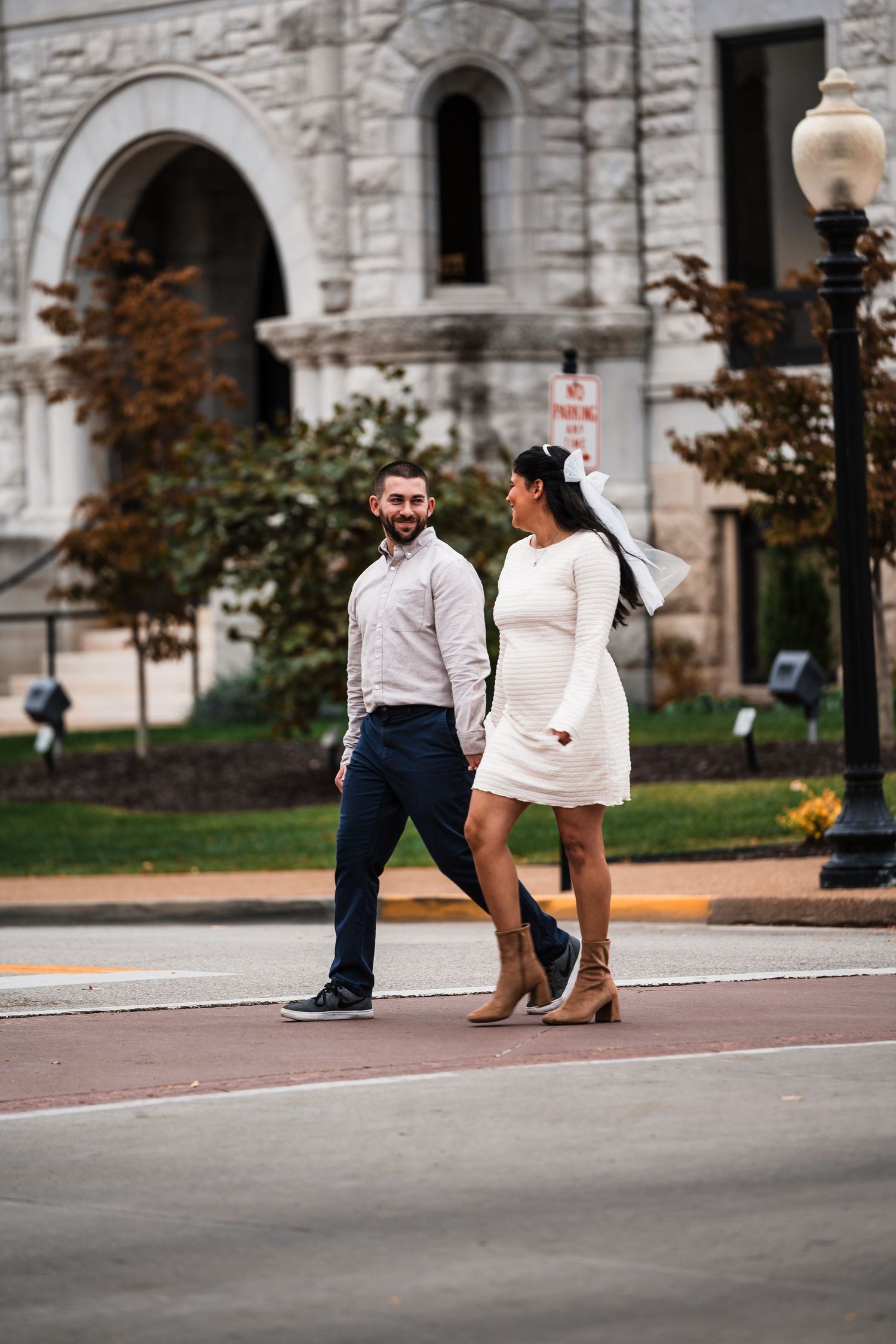 A couple walks hand in hand along a street with a stone church building in the background.