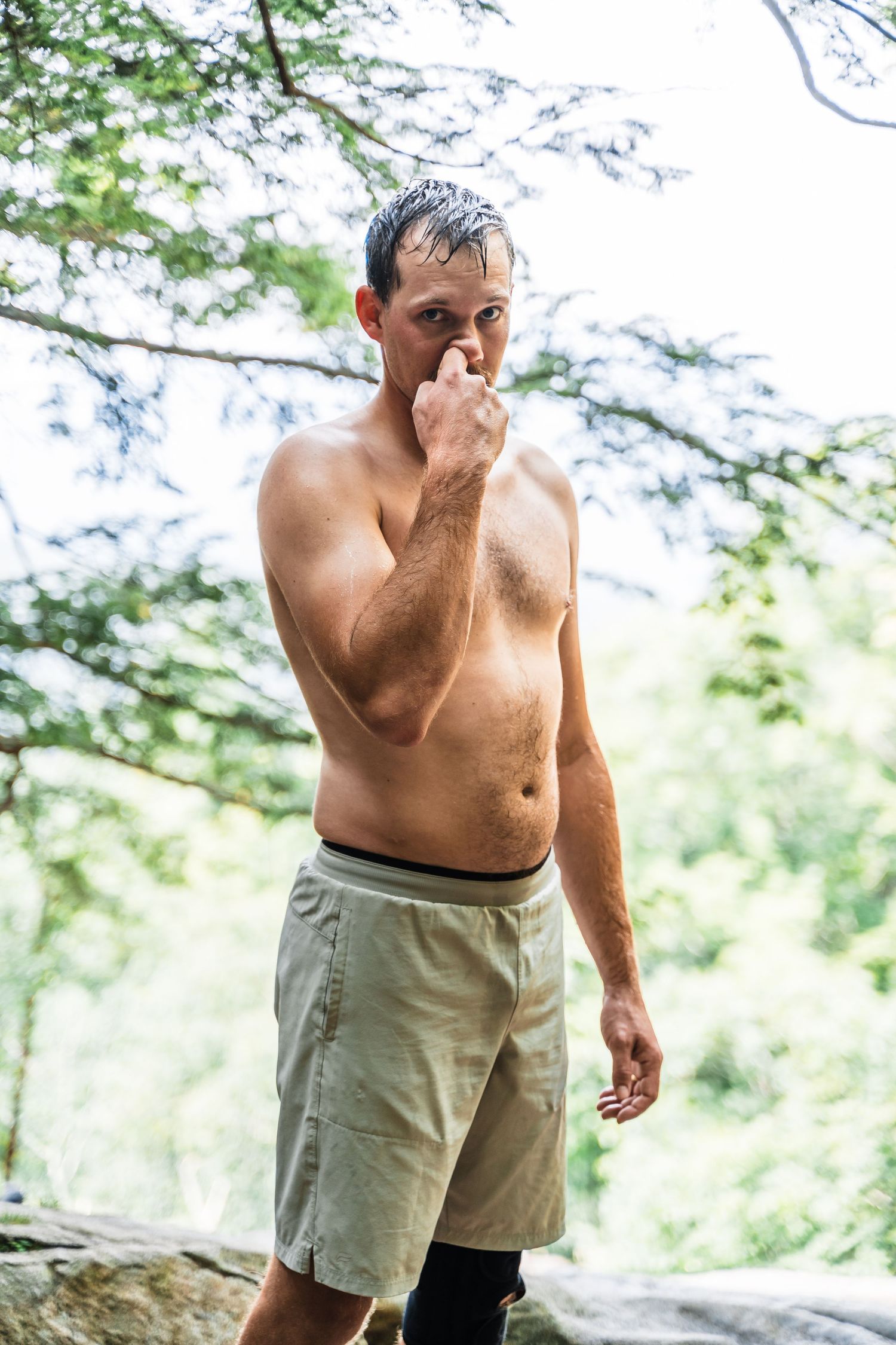 A shirtless hiker pauses to rest along a wooded trail on a summer day.