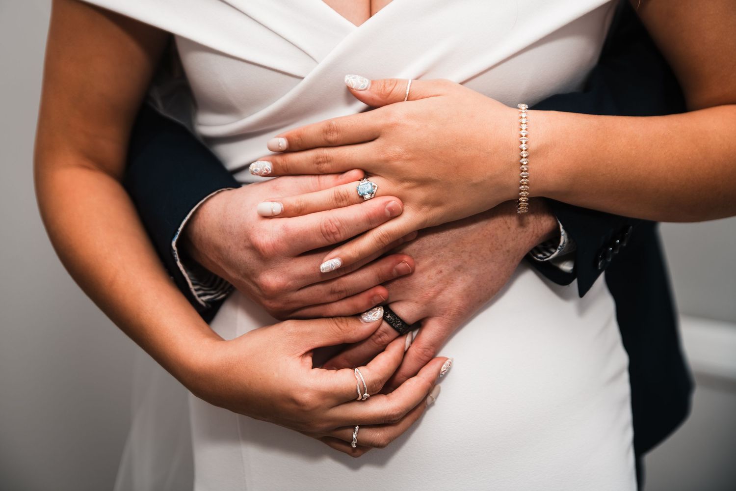 Close-up shot of hands with wedding rings intertwined against white dress fabric.