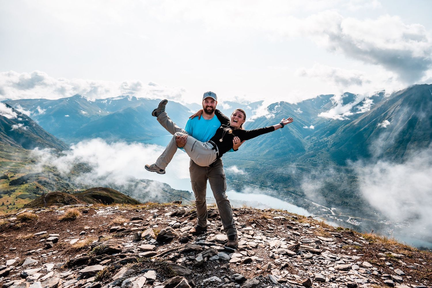 Adventurous couple celebrating on mountain summit with scenic valley views below.