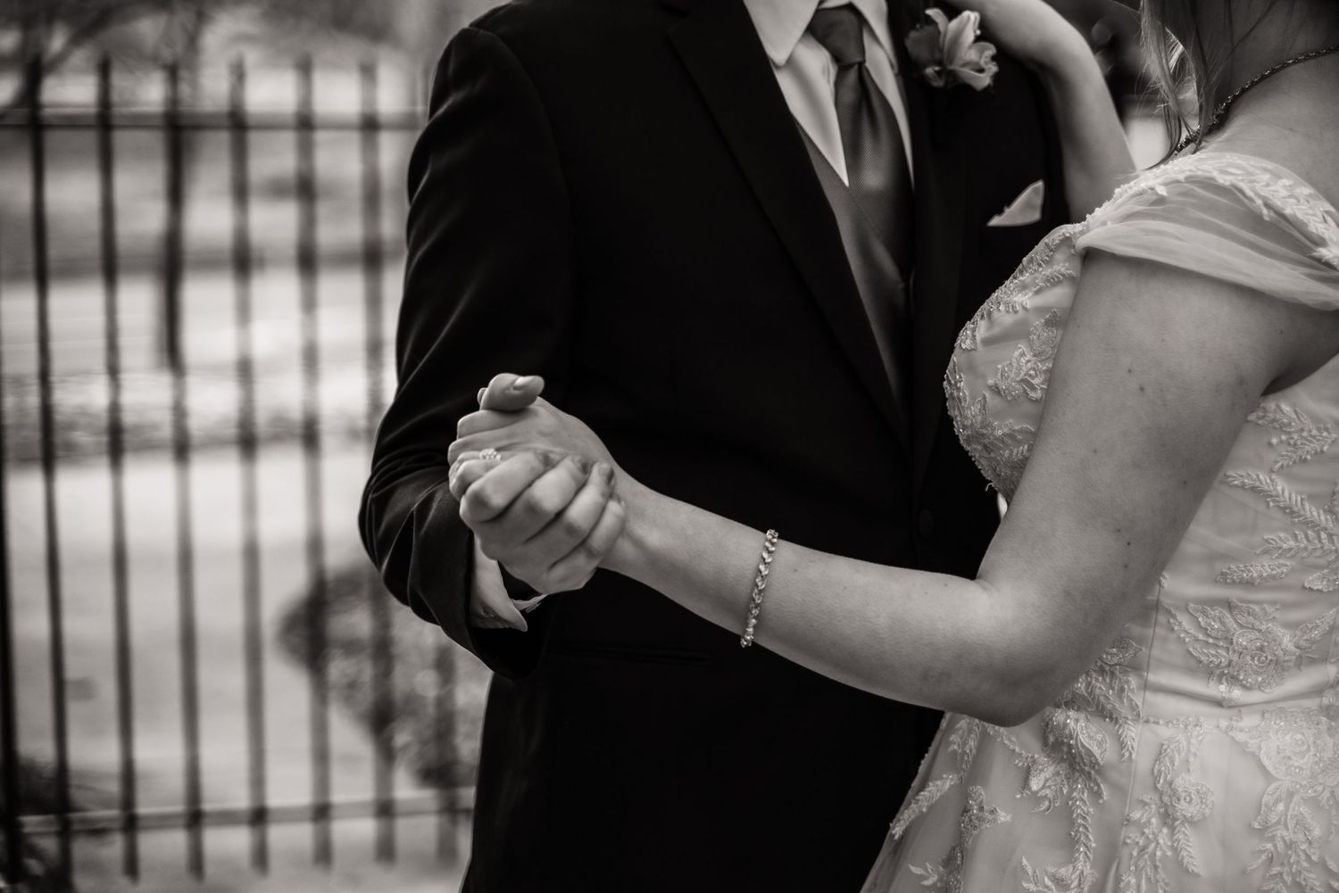 A black and white close-up of newlyweds' hands clasped together during their first dance.