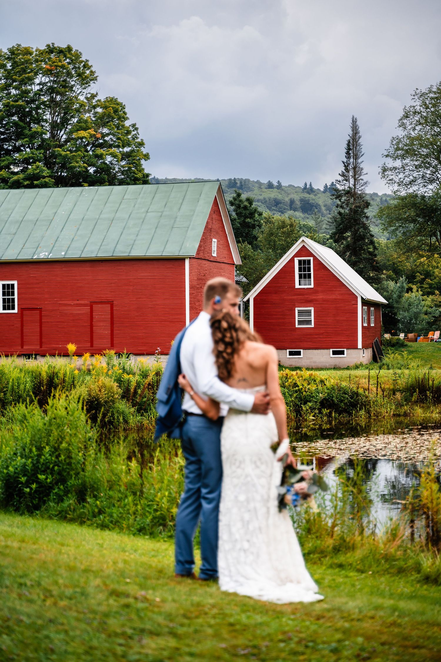 A wedding portrait in front of classic red barns with a green metal roof and mountain backdrop.