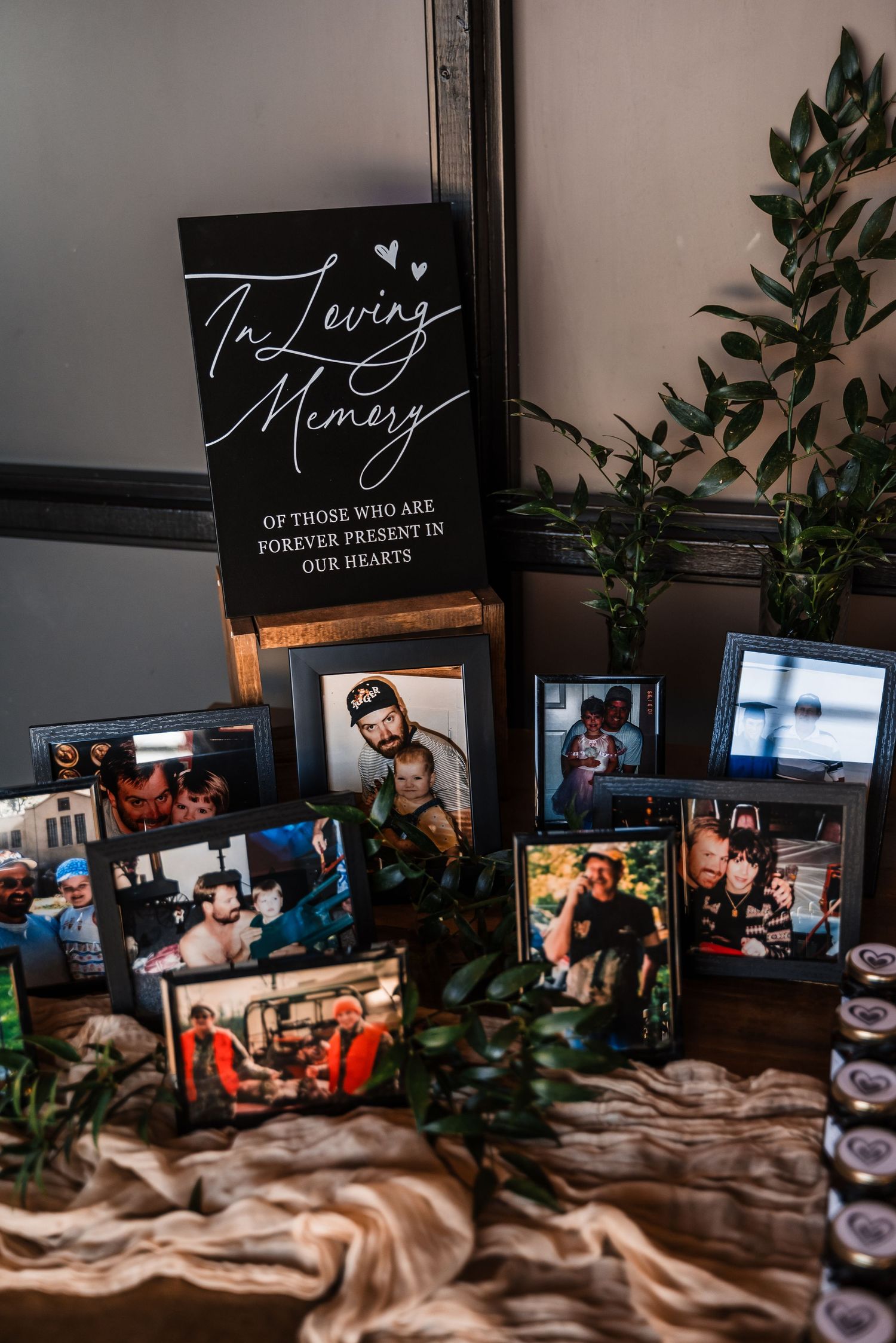 Memorial display with photos and text reading 'In Loving Memory' surrounded by greenery and fabric.