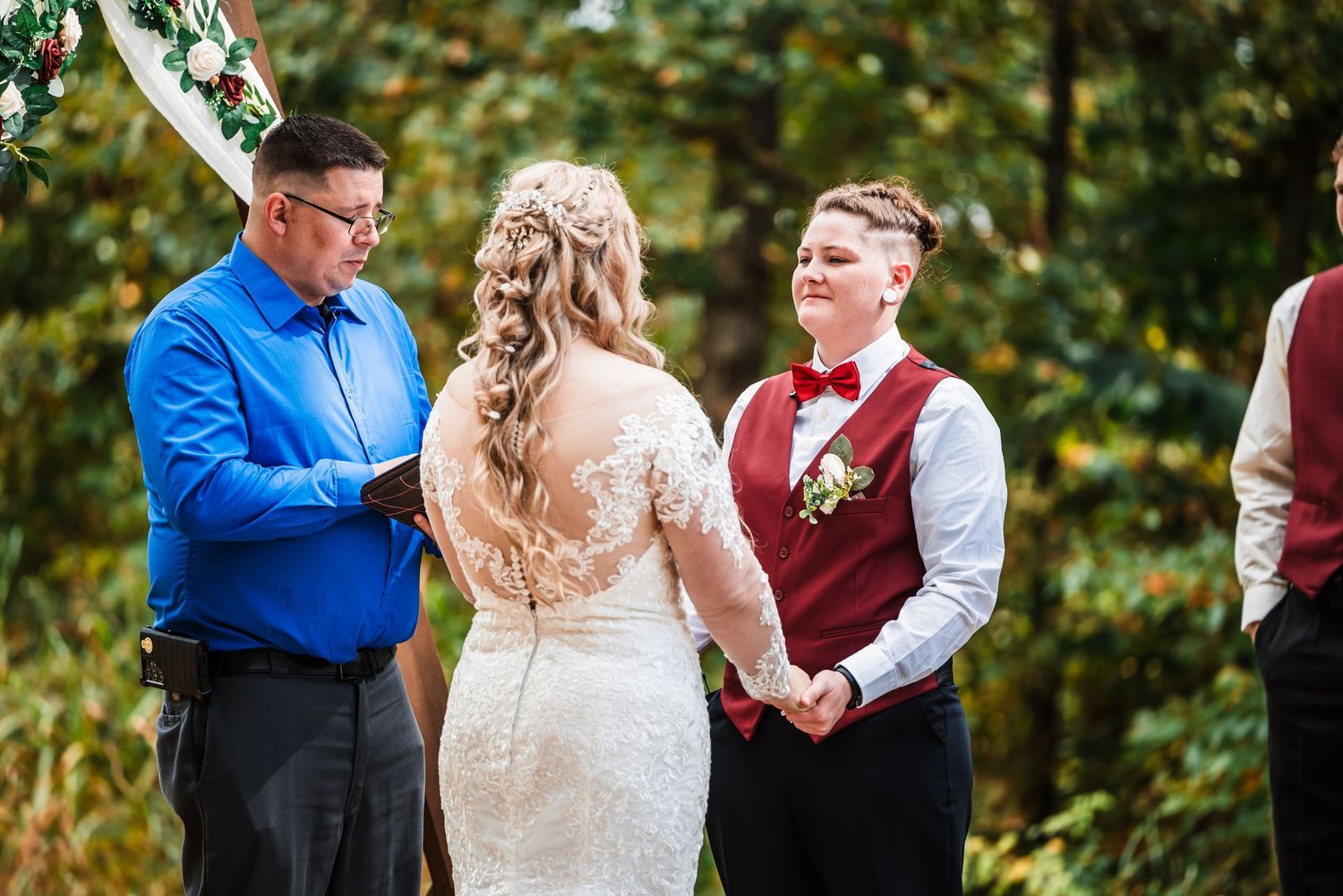 Outdoor wedding ceremony with couple and officiant surrounded by autumn foliage.