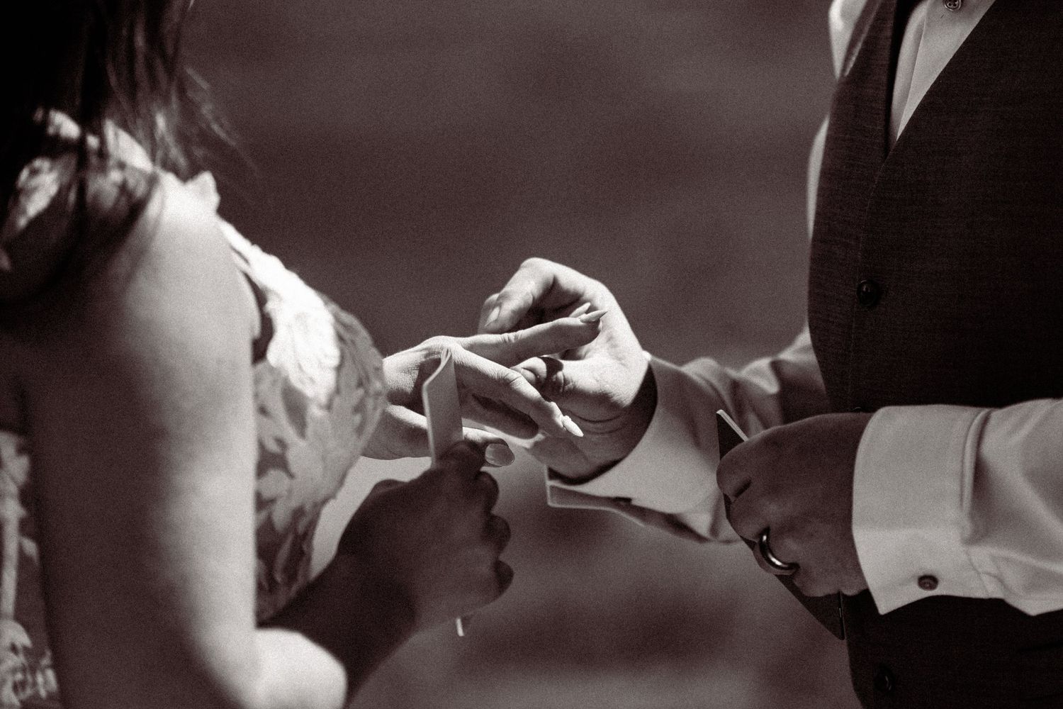 Groom placing wedding ring on bride's finger during ceremony, black and white close-up photo.