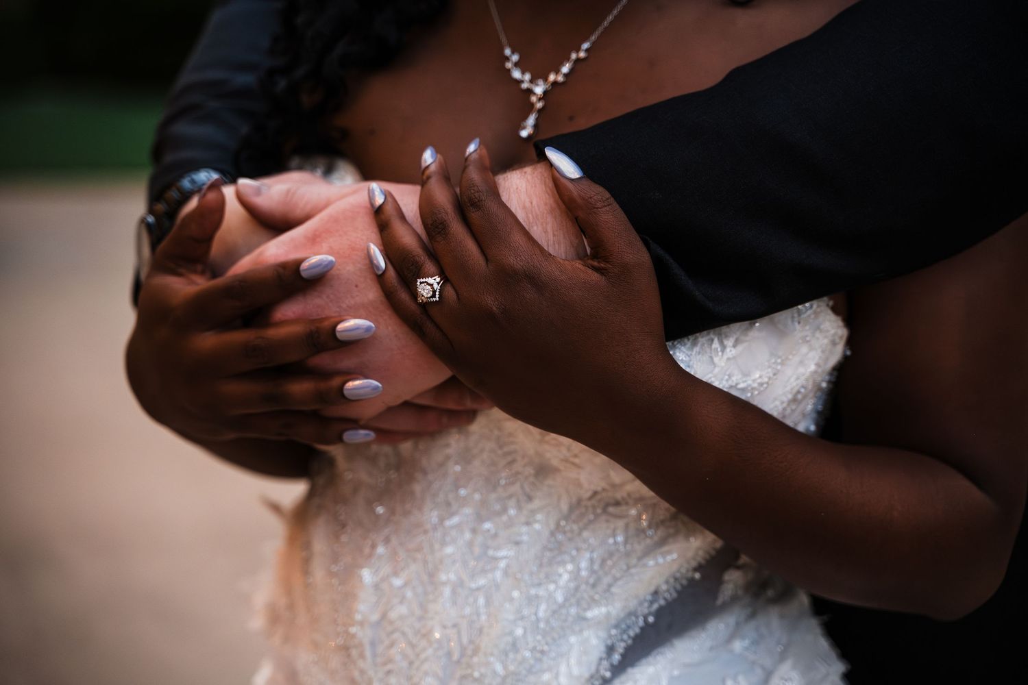 Close-up of couple holding hands showing engagement ring and manicured nails in wedding attire.