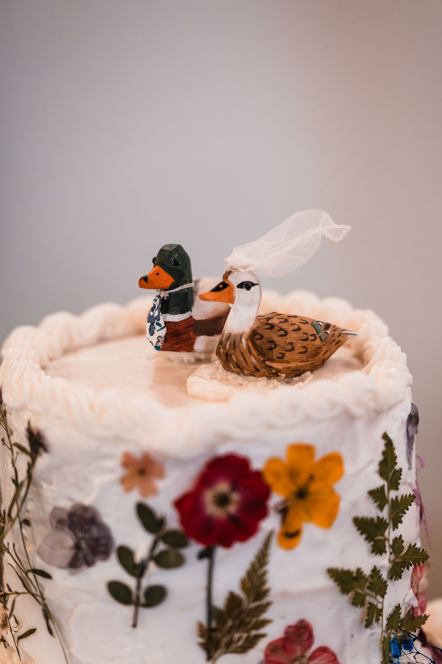Wedding cake topped with duck figurines dressed as bride and groom, decorated with pressed flowers.