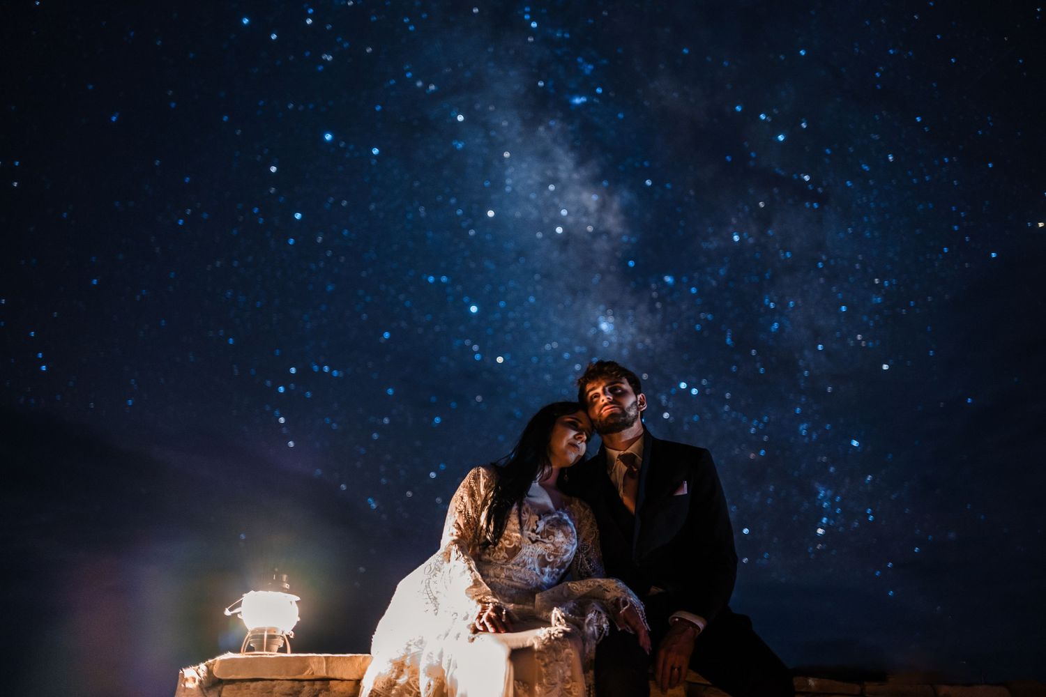 A couple poses under a starry night sky with glowing lanterns creating a romantic wedding photography scene.