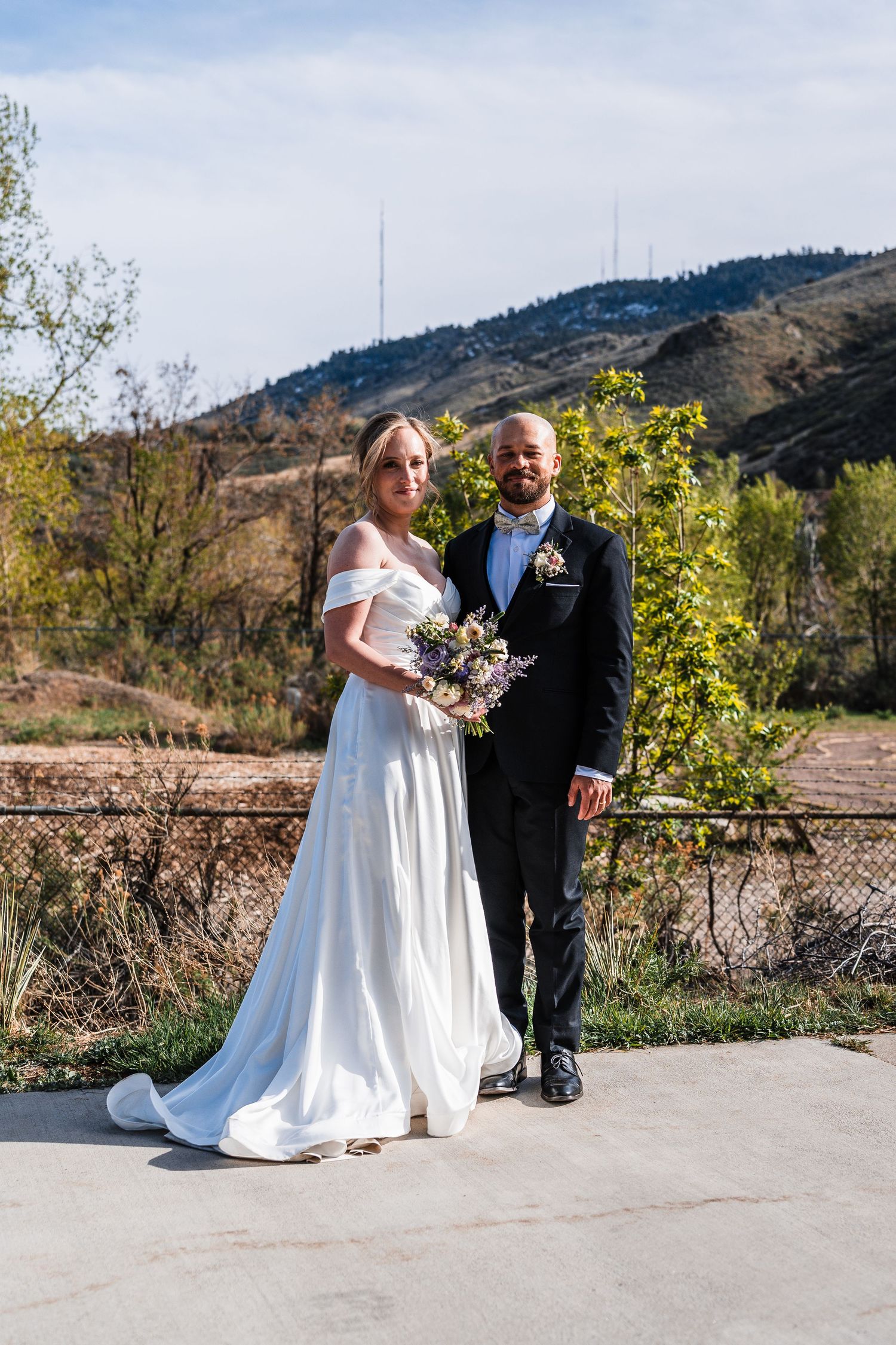 Bride and groom pose together outdoors with mountain landscape backdrop on wedding day.