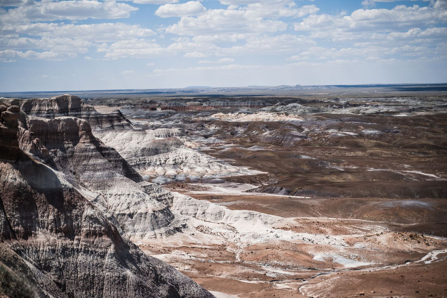 A dramatic desert canyon landscape shows white striped rock formations stretching to the horizon.