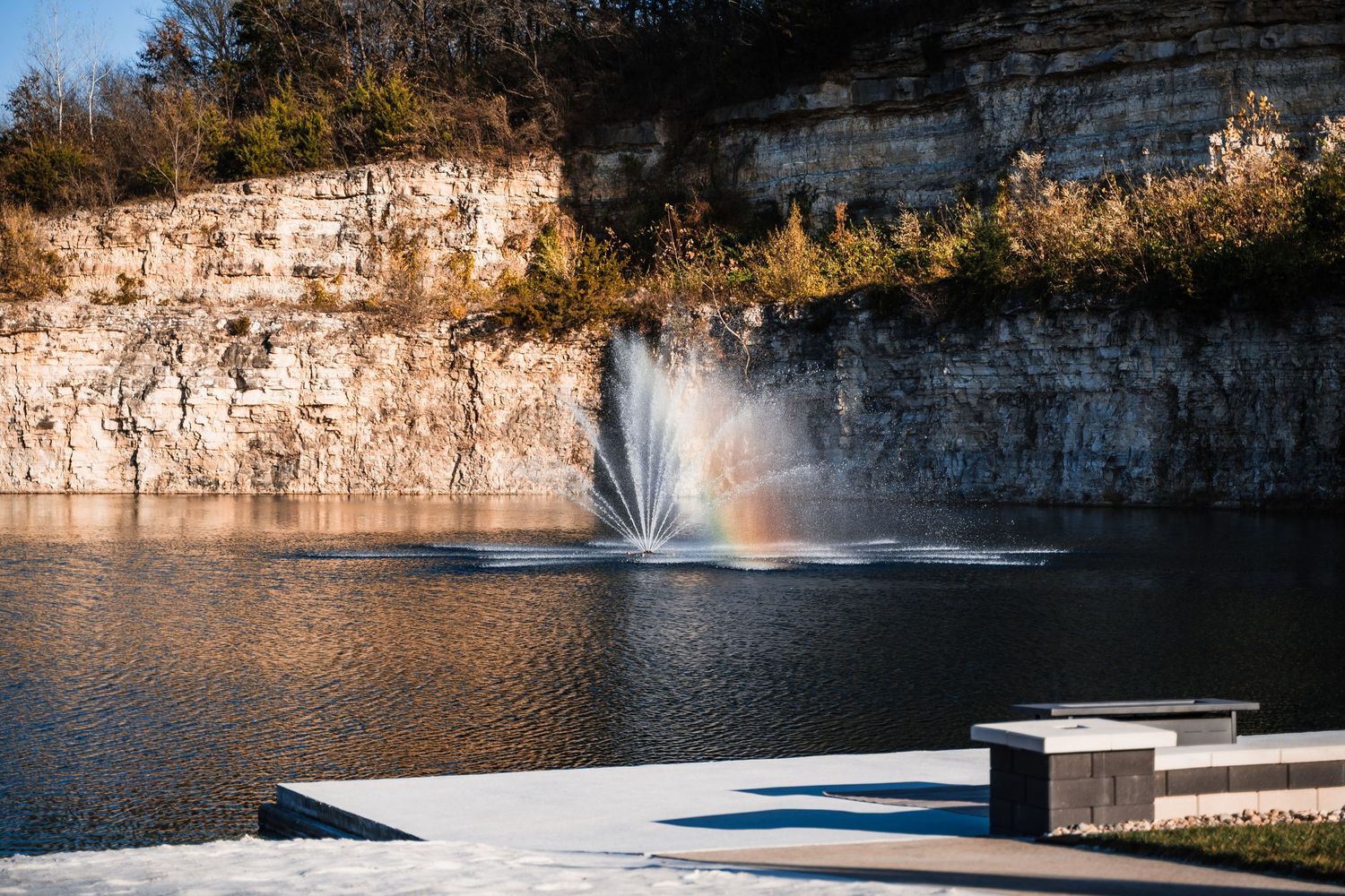 Scenic limestone cliffs and waterfalls along a riverbank with clear blue water reflecting the sunlight.