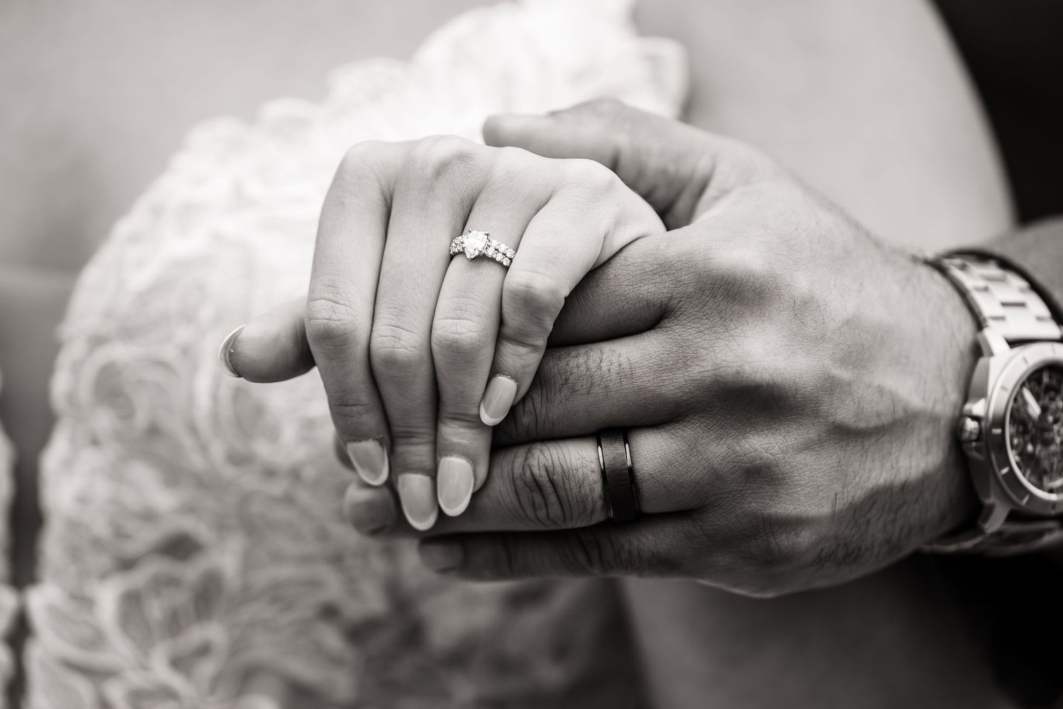 Close-up black and white photo of hands with wedding rings and elegant watch.