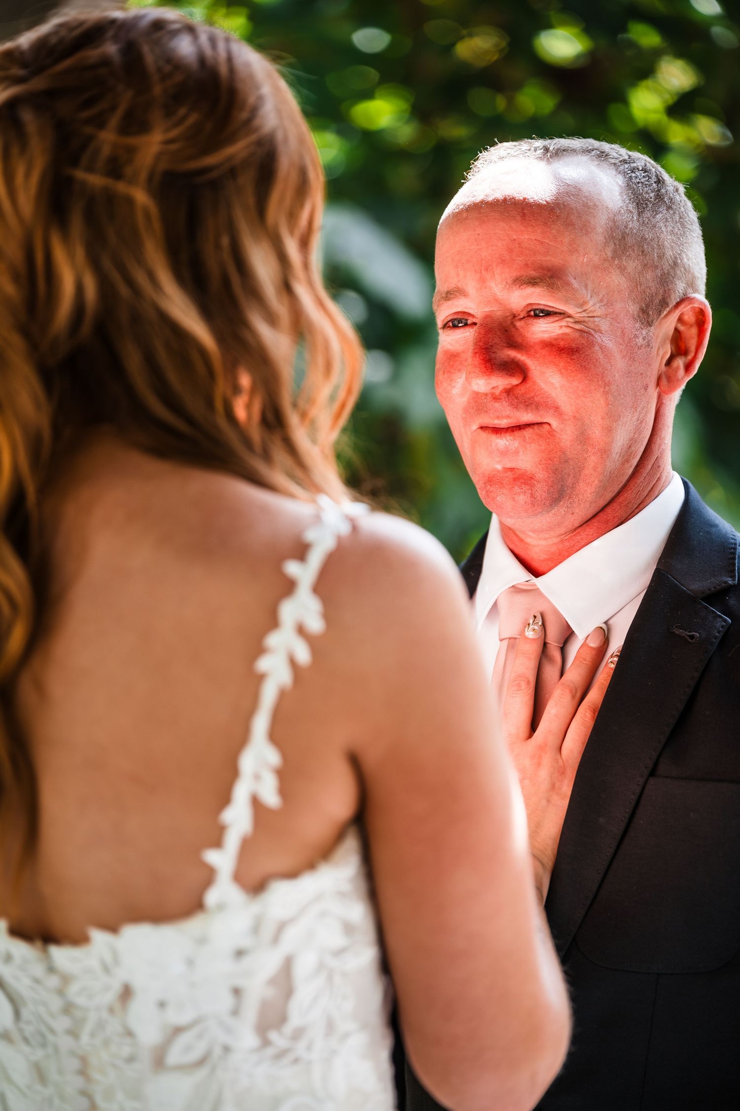Bride in white lace dress and groom share an emotional first look moment in a garden setting.