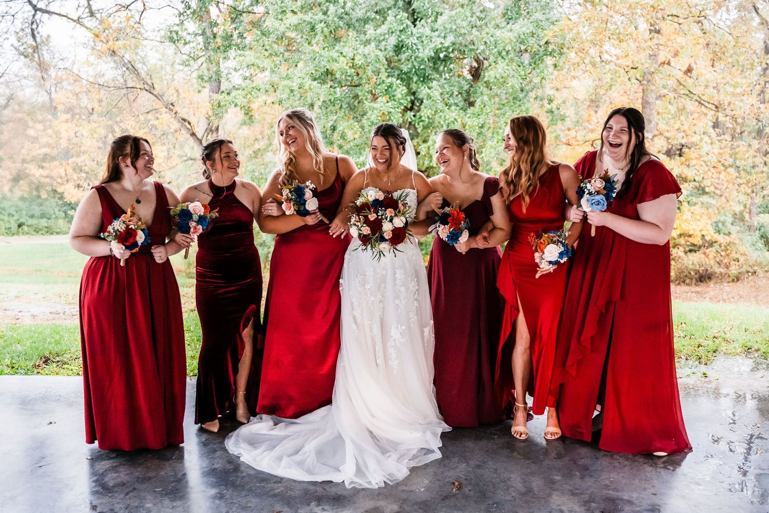 Wedding party in burgundy dresses poses outdoors during autumn.