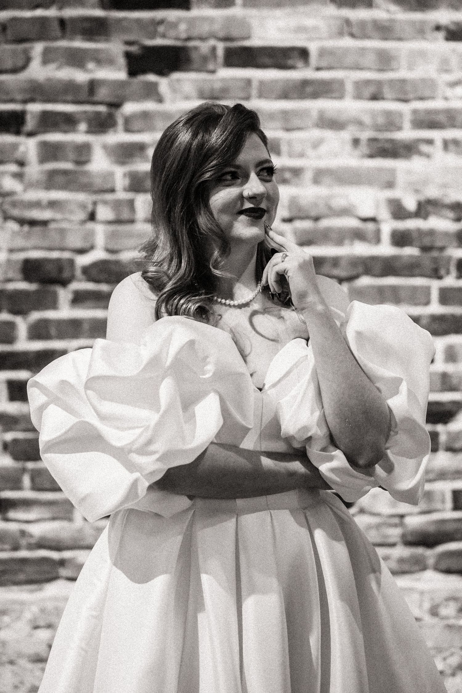 Black and white portrait of a bride in a romantic puff-sleeve wedding dress against brick wall.