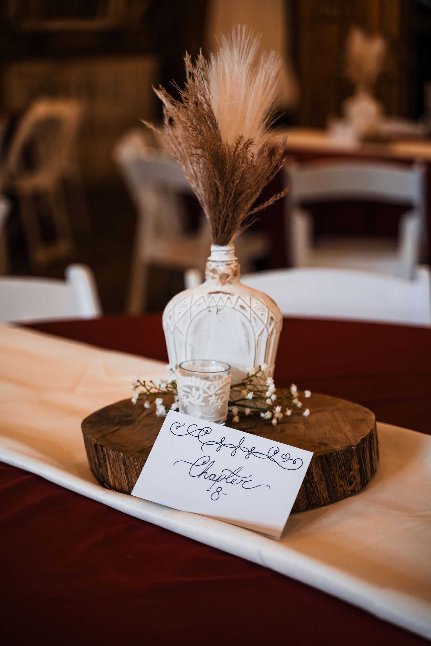 Rustic wedding centerpiece with dried pampas grass in a white bottle on a wooden slice.