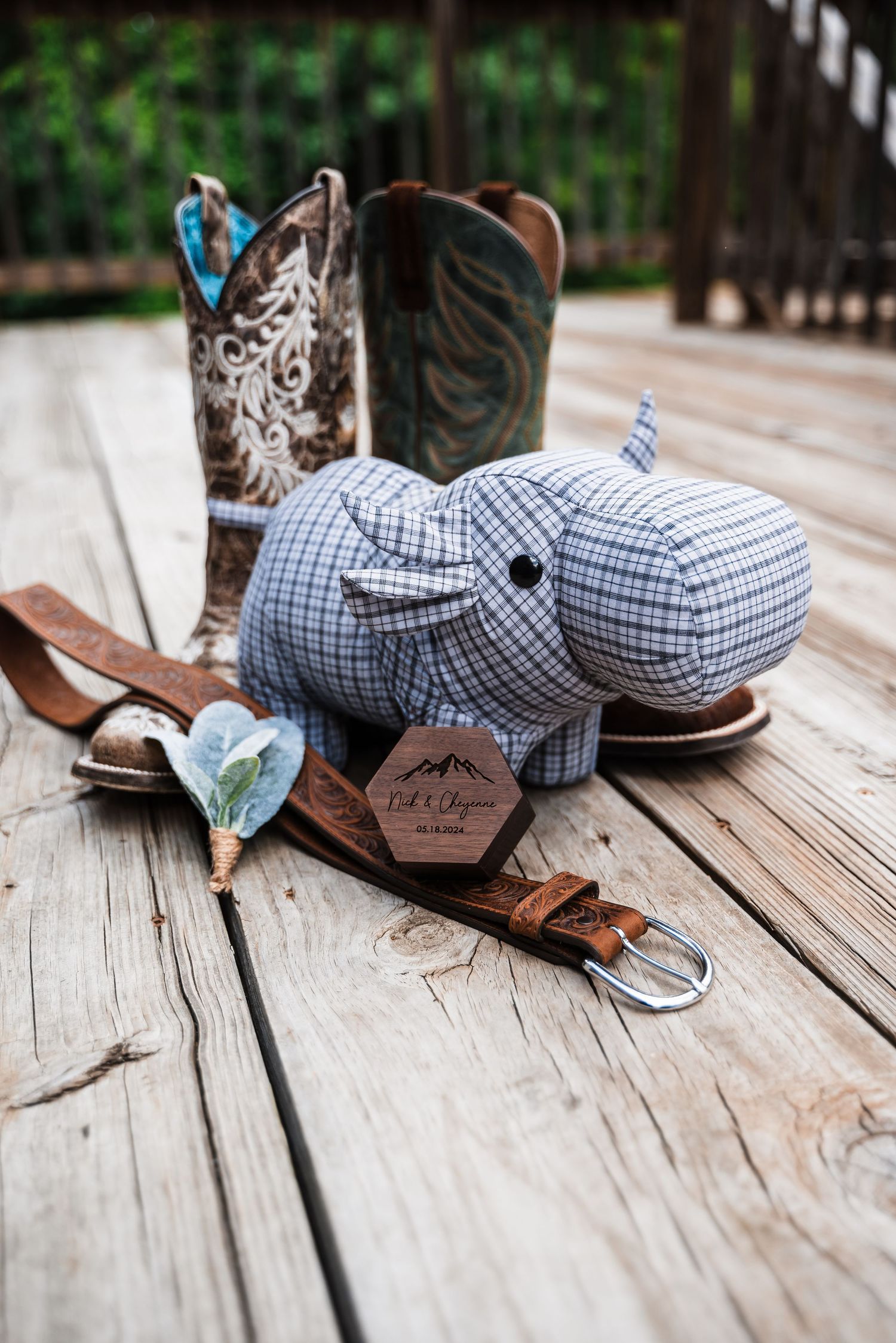 Wedding accessories including cowboy boots, checkered bow tie, and leather belt arranged on wooden decking.