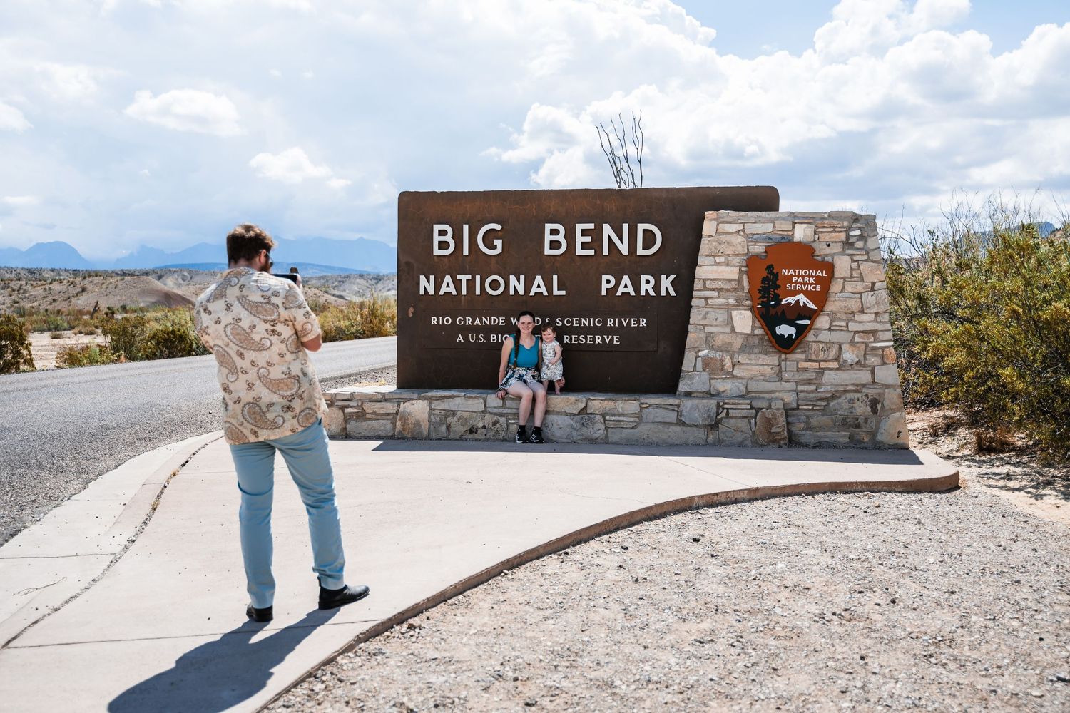 Visitors taking photos at the Big Bend National Park entrance sign with desert landscape in the background.