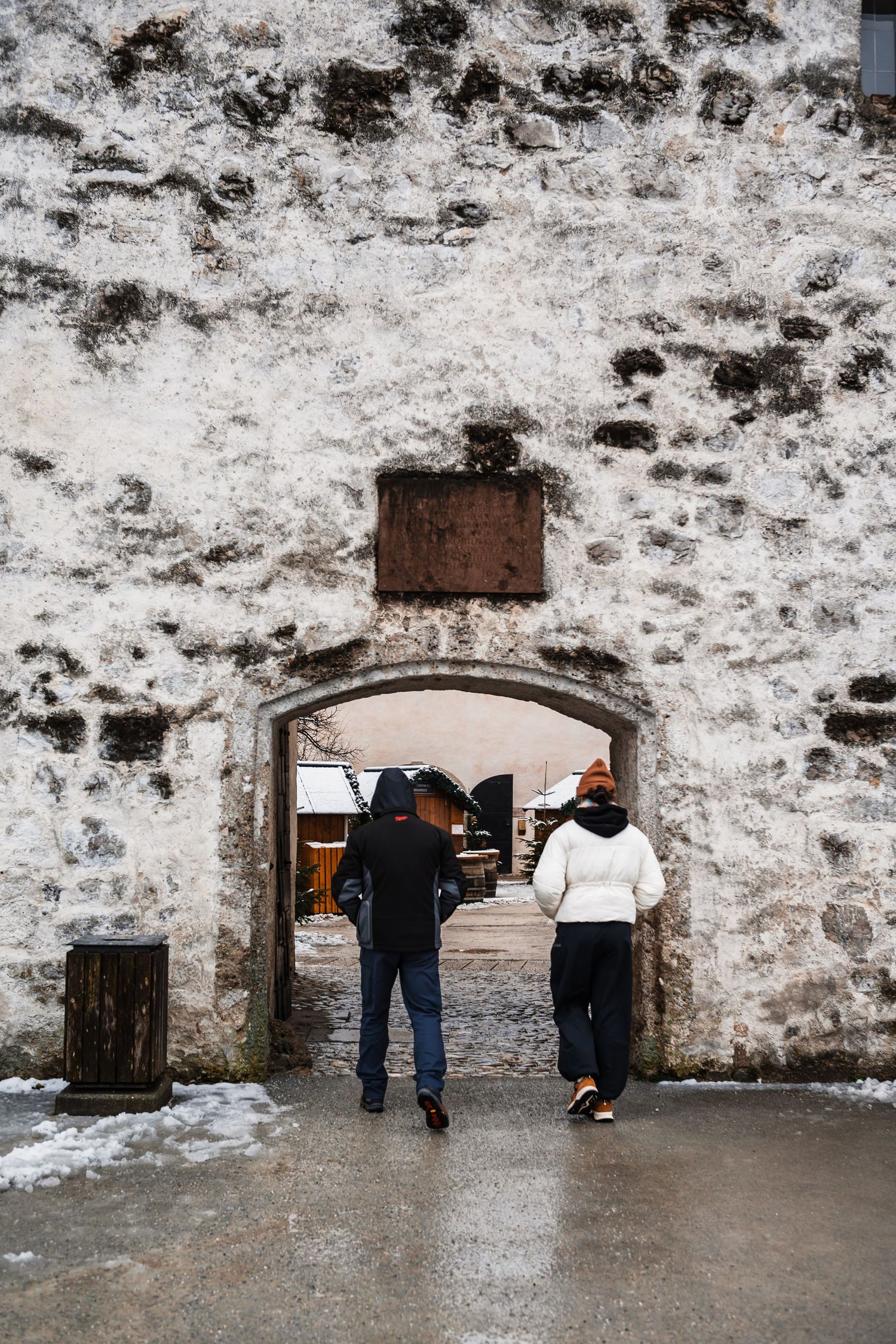 People walking through snow-covered stone archways of a historic fortress wall.