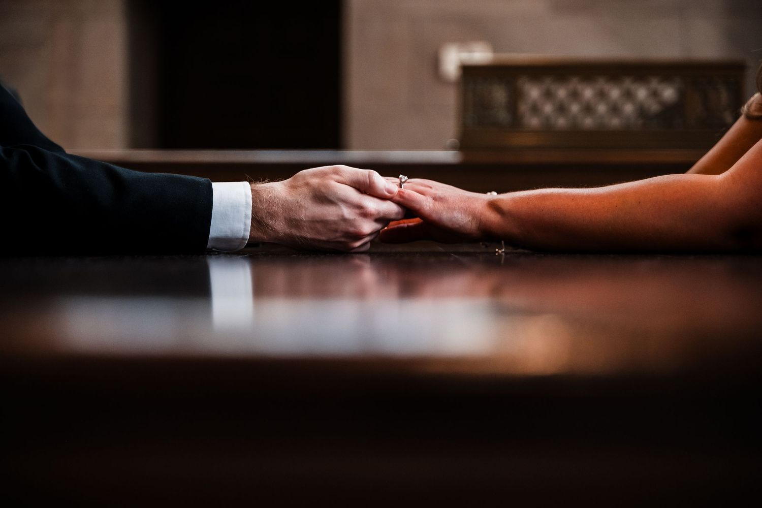 Hands of two people holding each other across a wooden table in a dimly lit setting.