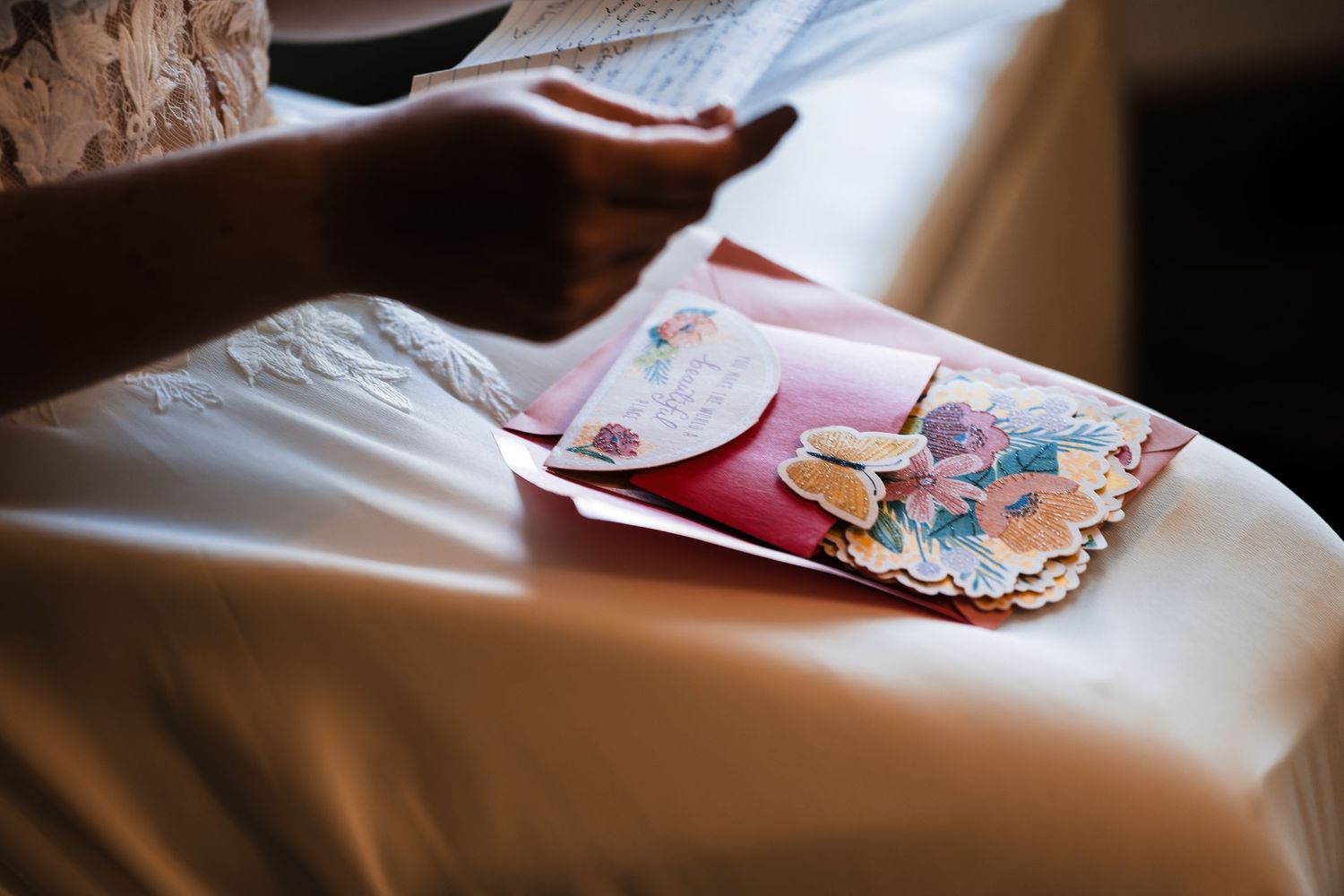 Bride reads heartfelt letter while holding floral cards before wedding ceremony.