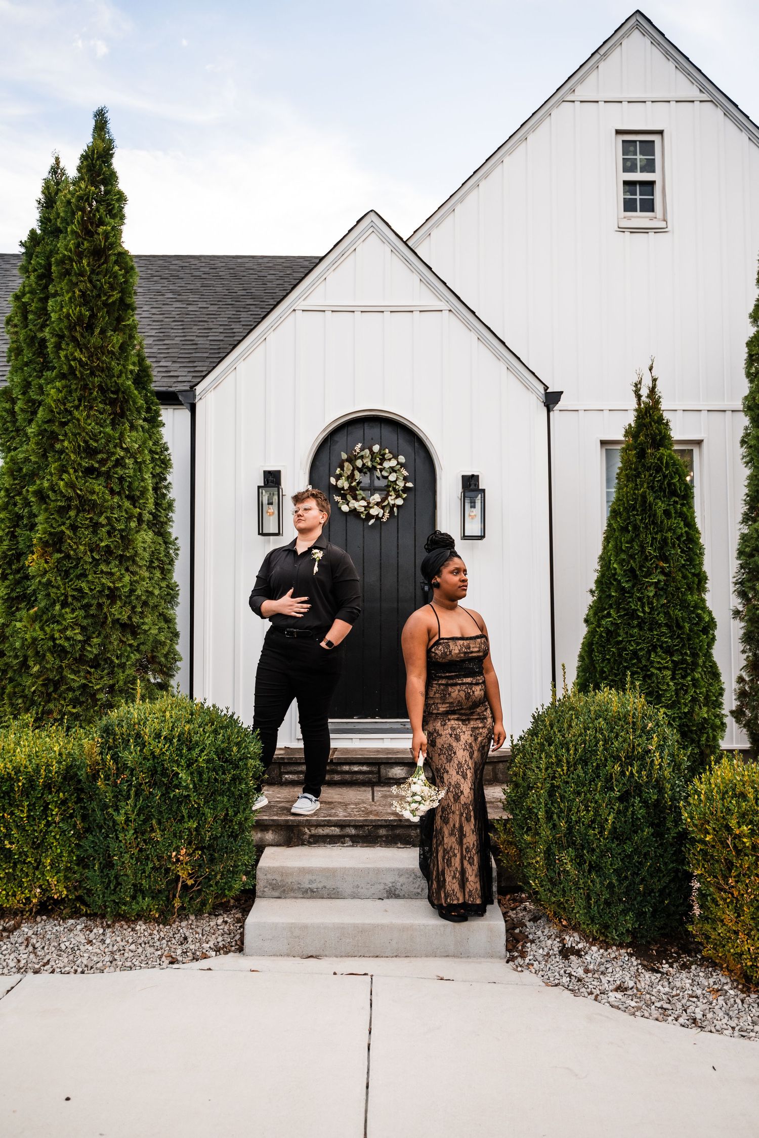 Modern white chapel exterior with black door and evergreen shrubs in a minimalist architectural design.