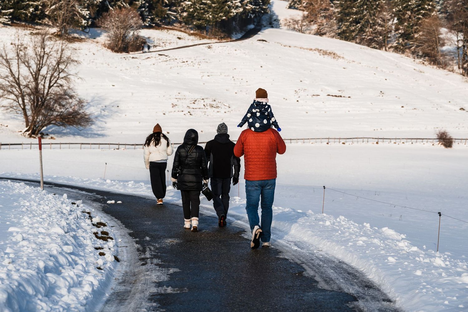 A group of people walking along a snowy winter path with one person carrying someone on their shoulders.