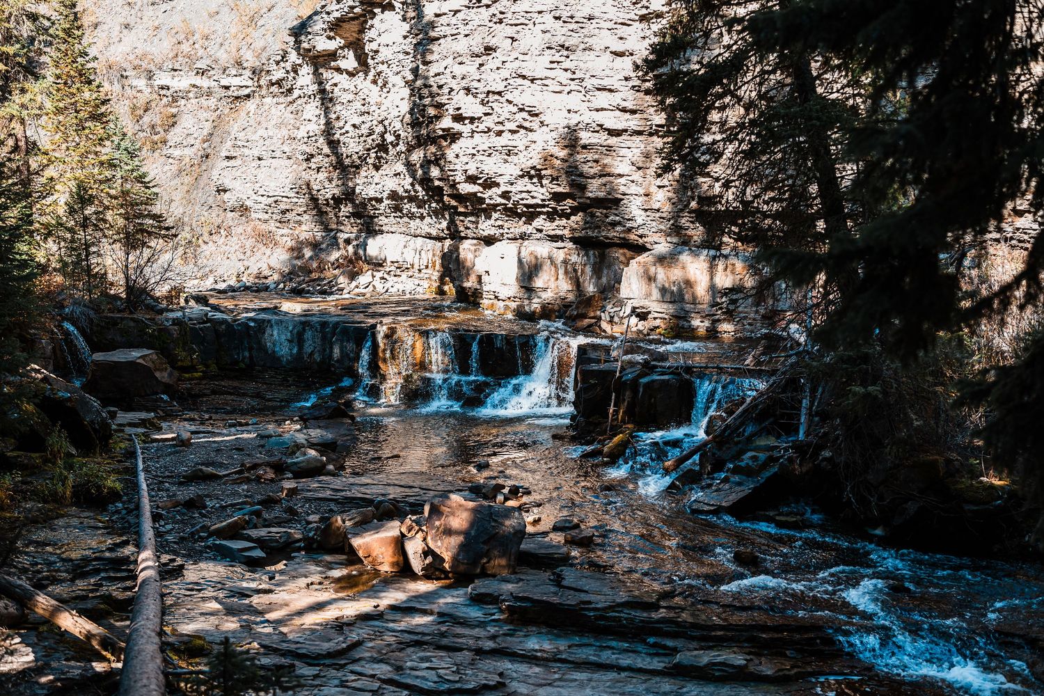 Scenic waterfall cascades down rocky cliffs in a forest setting with bright blue water and natural stone formations.