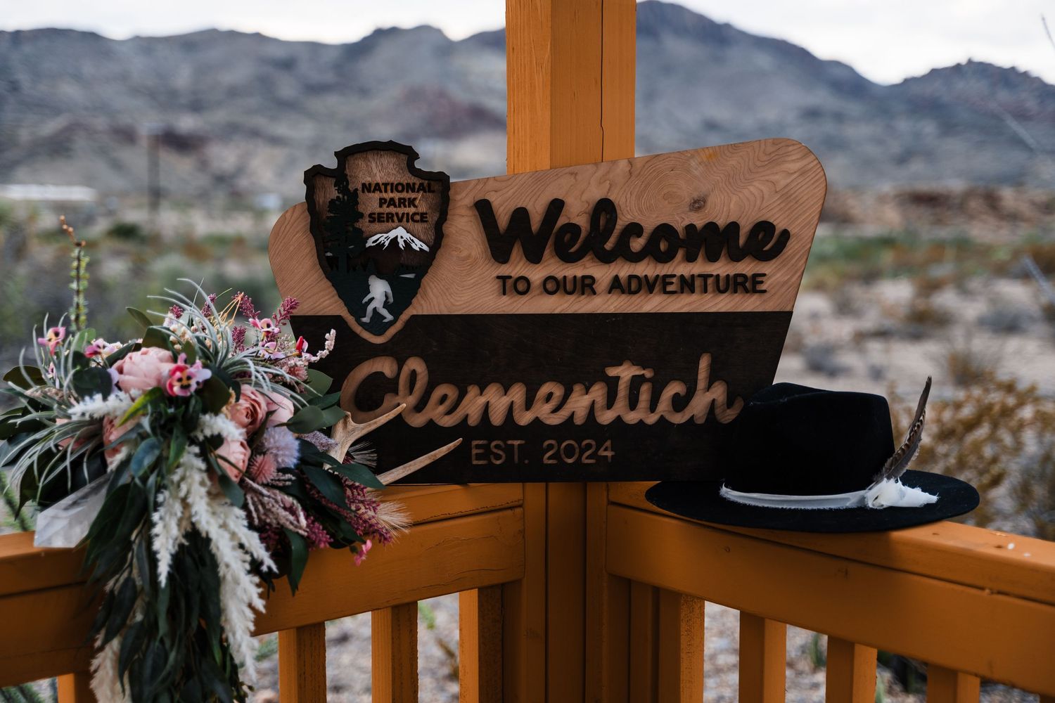 National Park Service welcome sign with wedding decorations and hat in desert setting.
