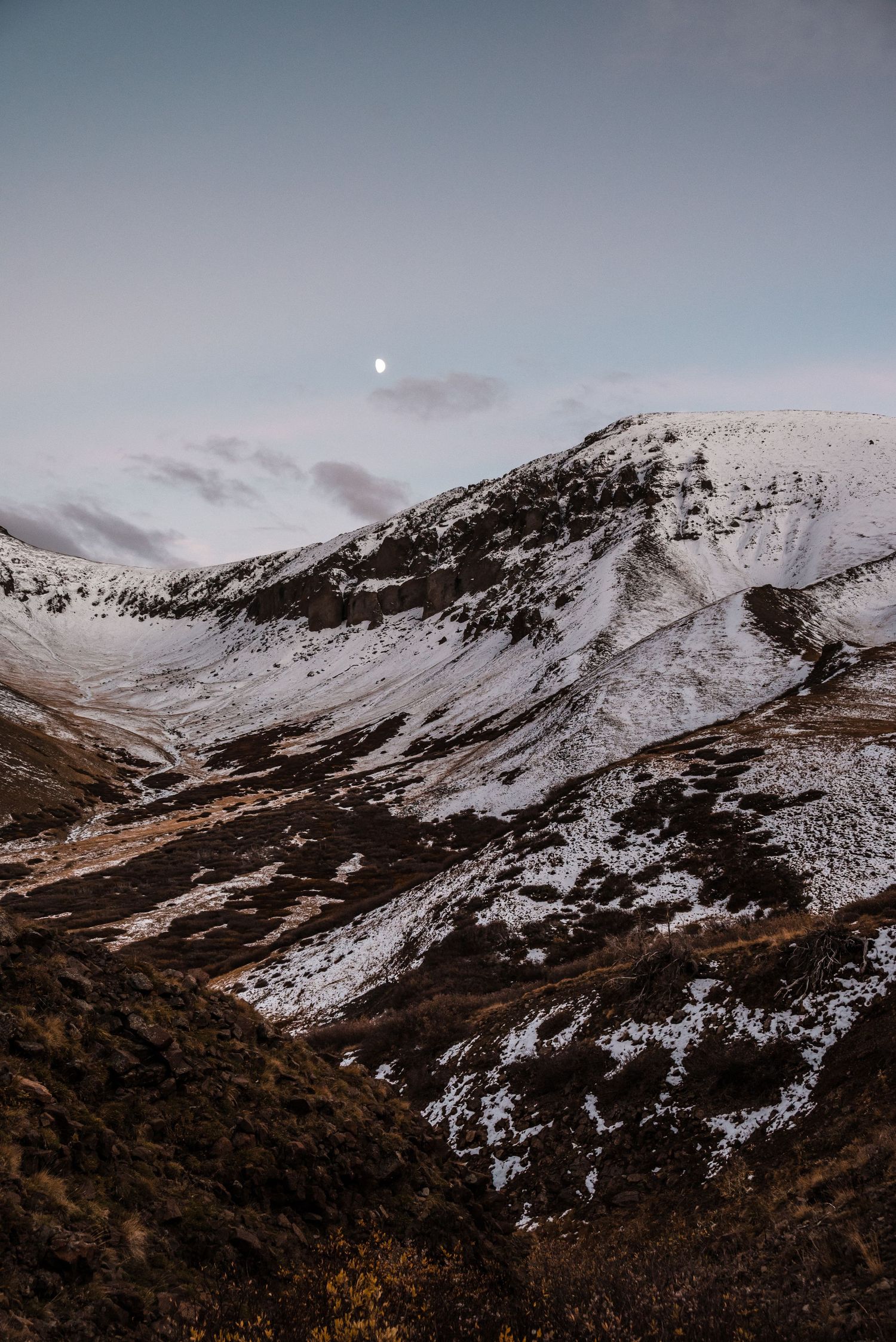 Moonlit mountain landscape with snow-covered peaks and valleys against a dusky sky in winter.