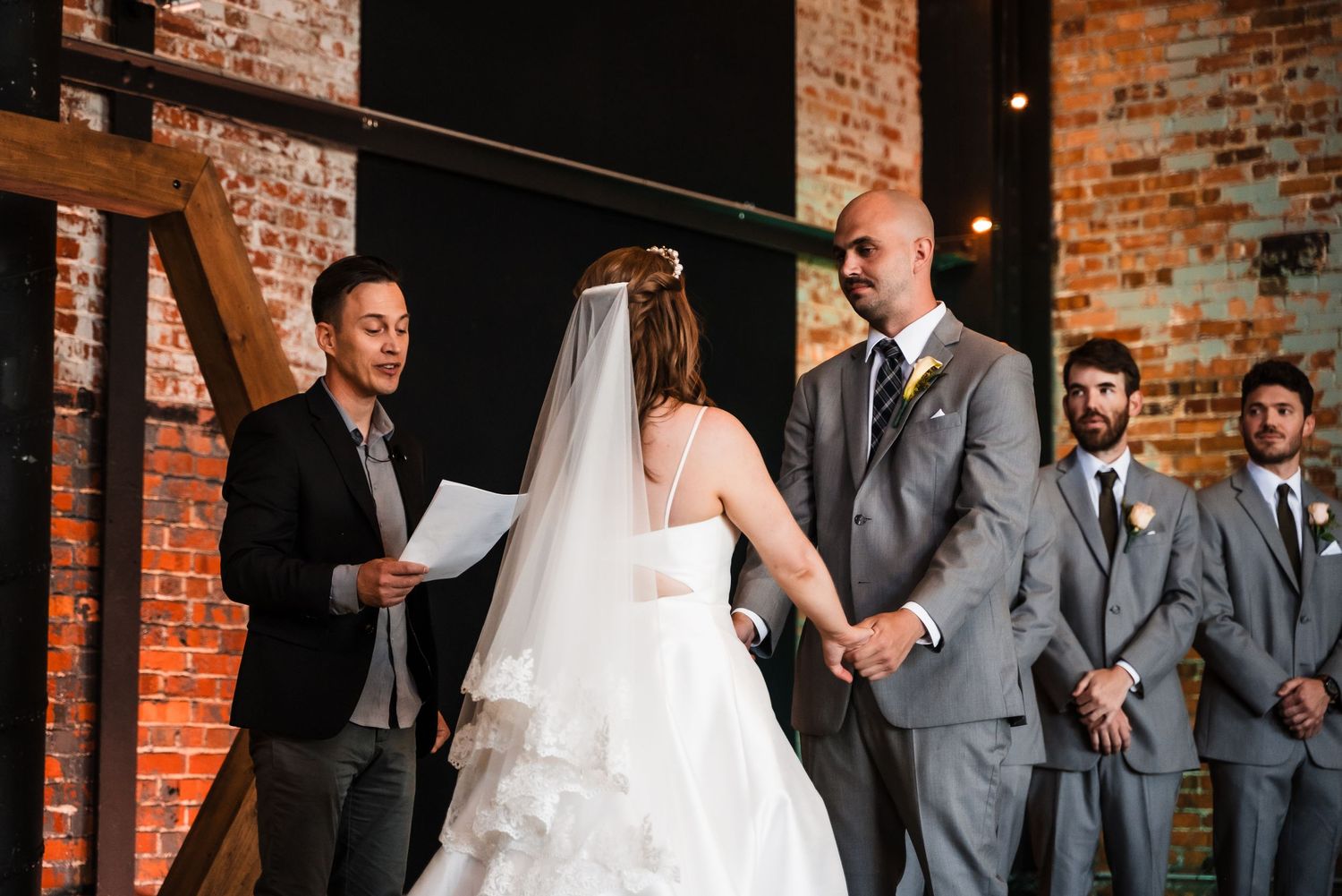 Wedding ceremony taking place in a rustic brick venue with warm lighting and elegant decor.