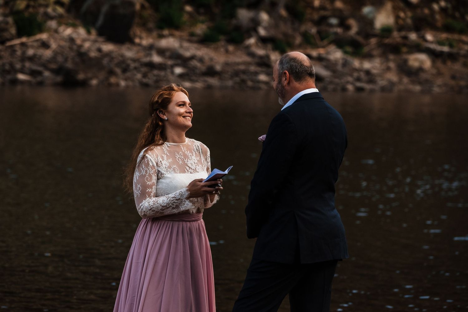 An intimate ceremony moment by a lake with forest and mountain scenery.
