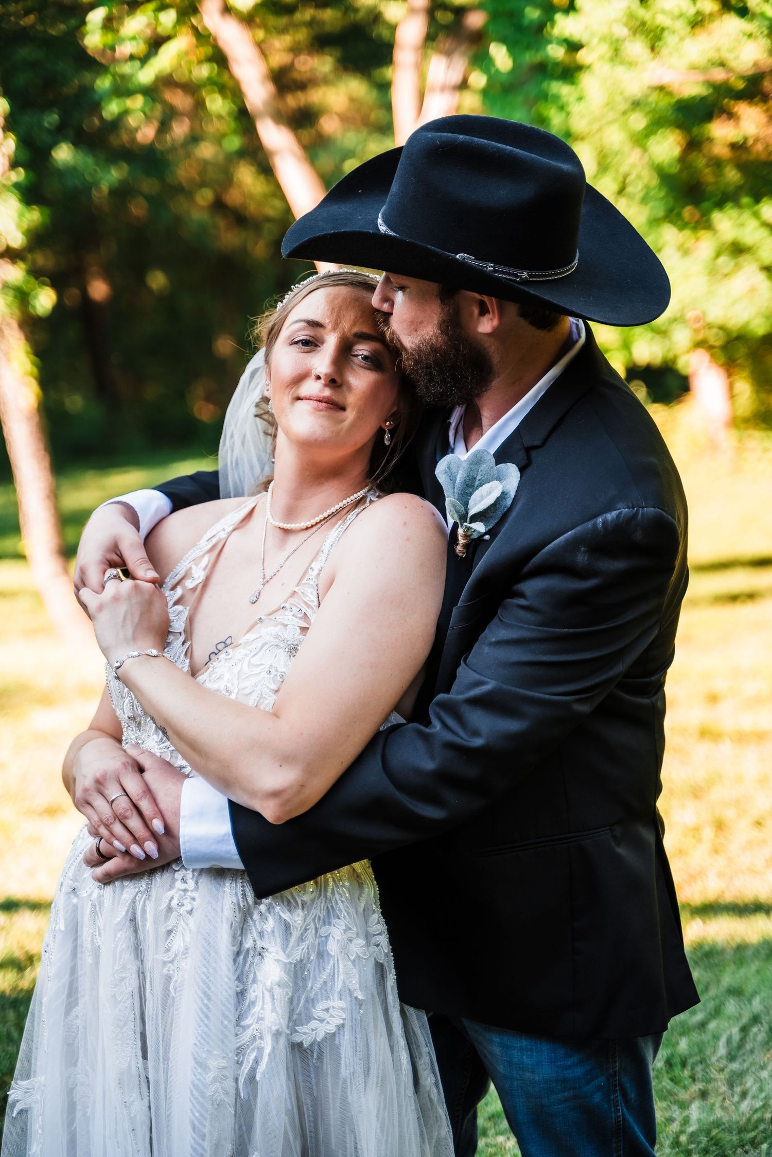 A romantic wedding portrait showing a couple embracing outdoors with the groom wearing a black cowboy hat.