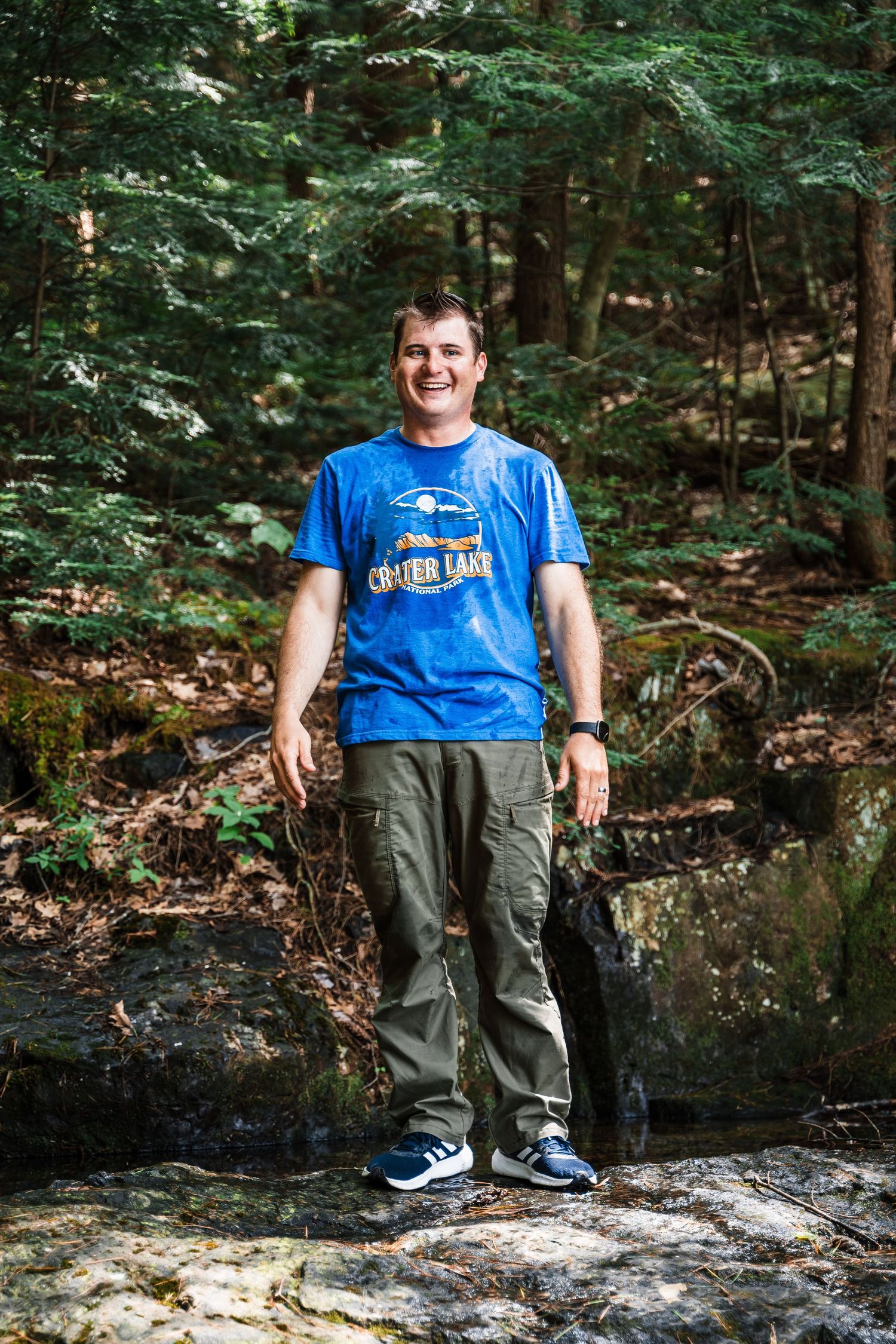 A hiker stands on a rocky outcrop surrounded by dense green forest.